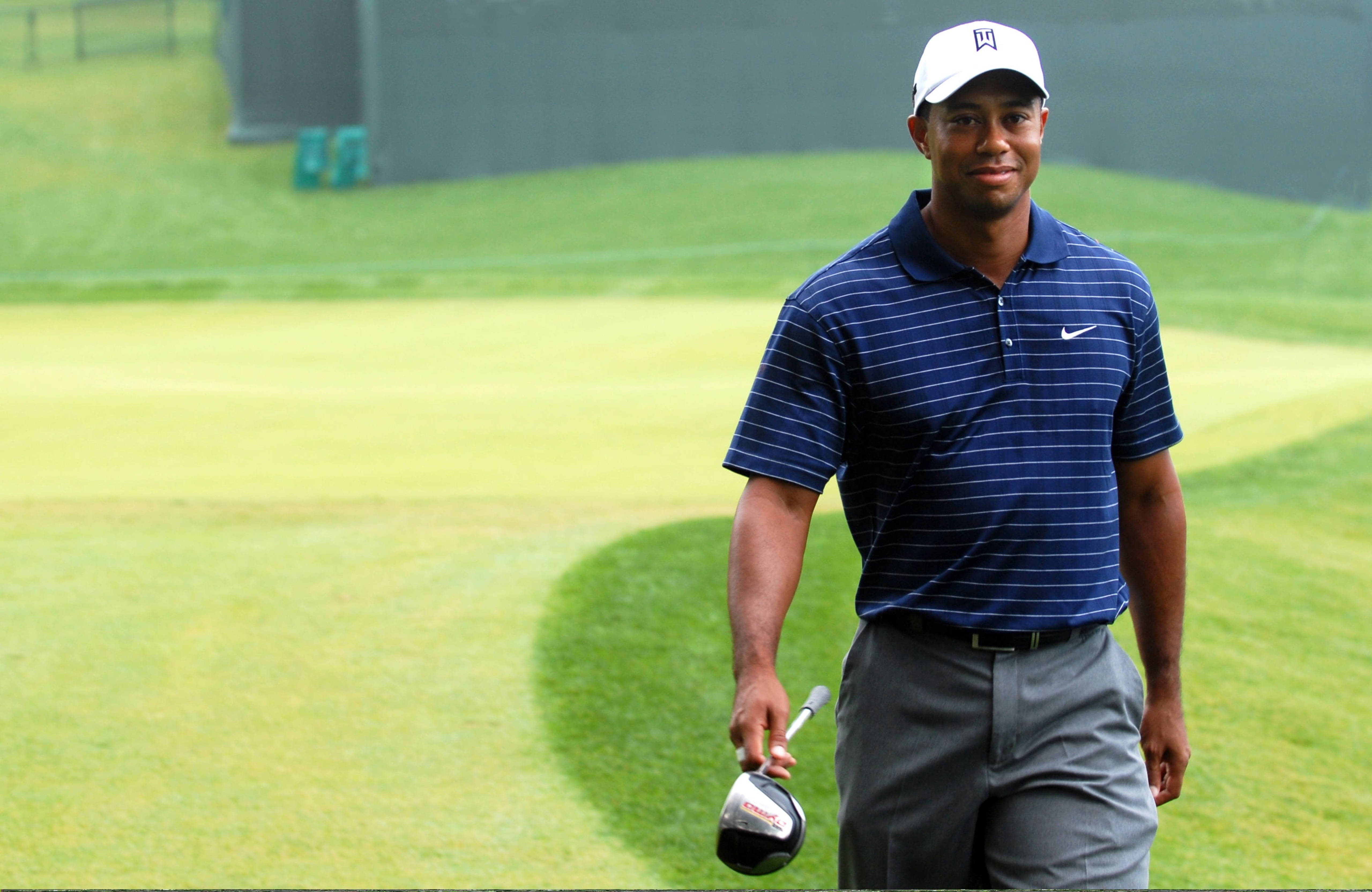 Tiger Woods 高爾夫名人 壁紙 — 老虎活士在明亮的日光下自信地走在翠綠的高爾夫球場上，手持一號木桿。