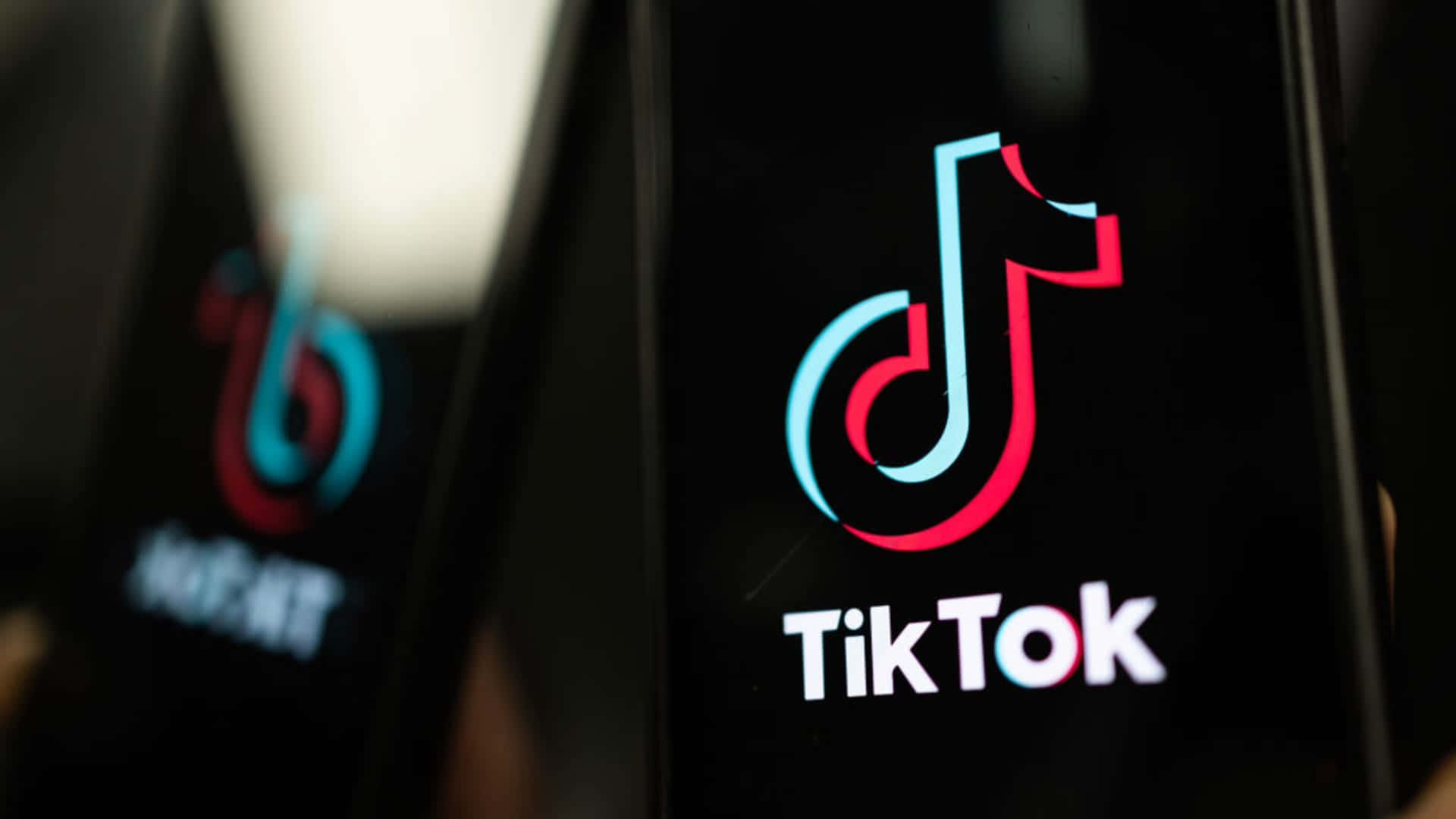 TikTok 為所有人準備了精彩內容！ 壁紙 — TikTok應用程式標誌在昏暗環境中於智能手機屏幕上發光的特寫。