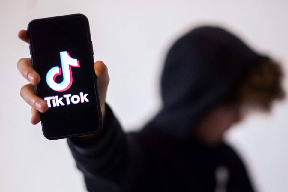 穿著黑色連帽衫的人手持顯示TikTok標誌的手機。