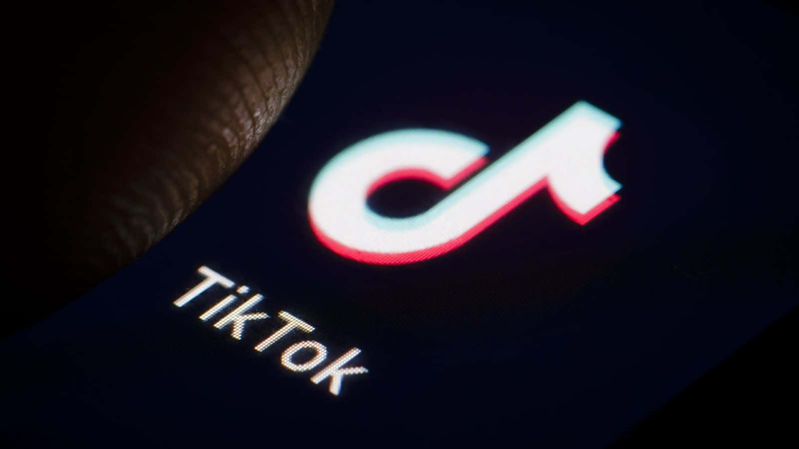 手指觸摸黑暗手機屏幕上發光的TikTok標誌