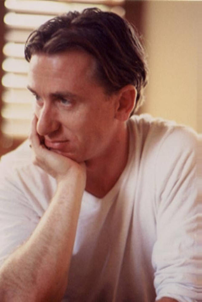 Tim Roth 愛慕凝視特寫 壁紙 — 一個穿著白色T恤的男人，托著下巴，若有所思地望向旁邊，光線柔和溫暖。