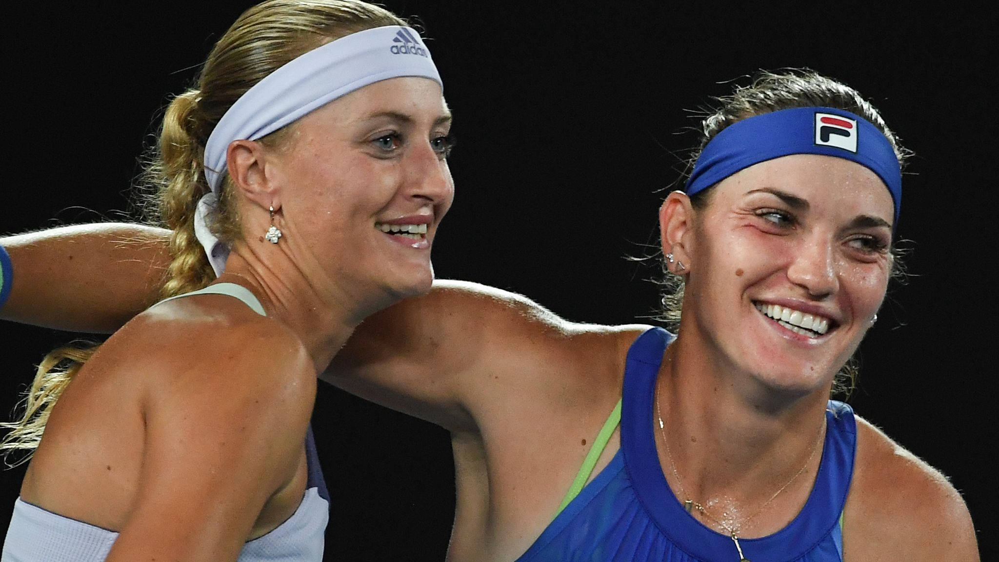 雙打組合 Timea Babos 與隊友 壁紙 — 兩位微笑的女網球運動員在比賽中於深色背景下熱情擁抱。
