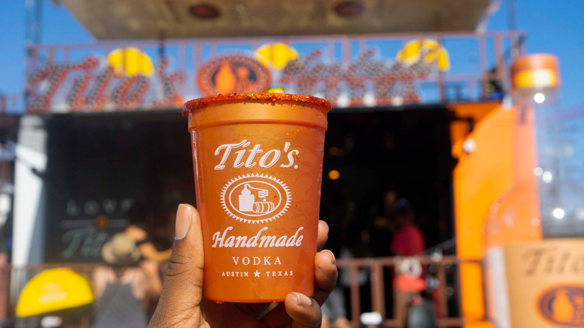 在陽光明媚的戶外節日中，手拿著Tito's伏特加飲料。