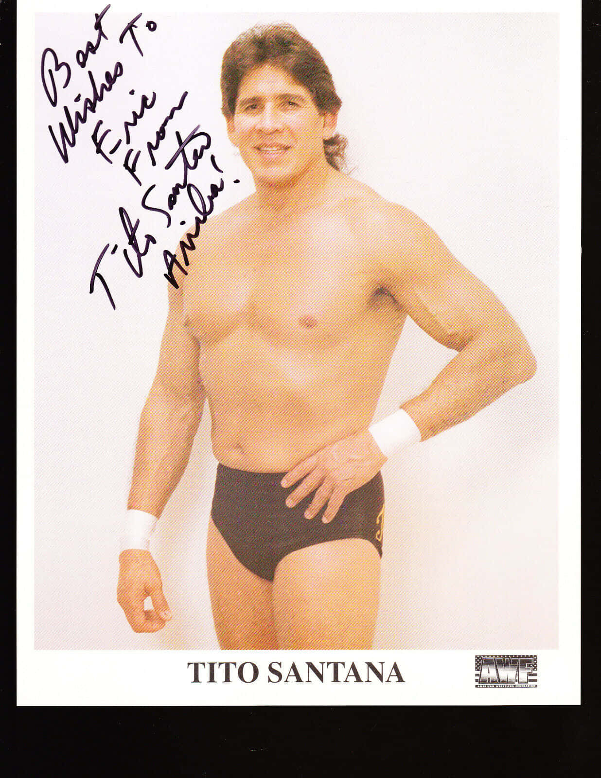 Tito Santana 簽名 WWF 海報 壁紙 — 赤裸上身的摔角手 Tito Santana 自信地擺姿勢，身穿黑色三角褲和白色護腕，背景為純白色，並附有他的簽名。