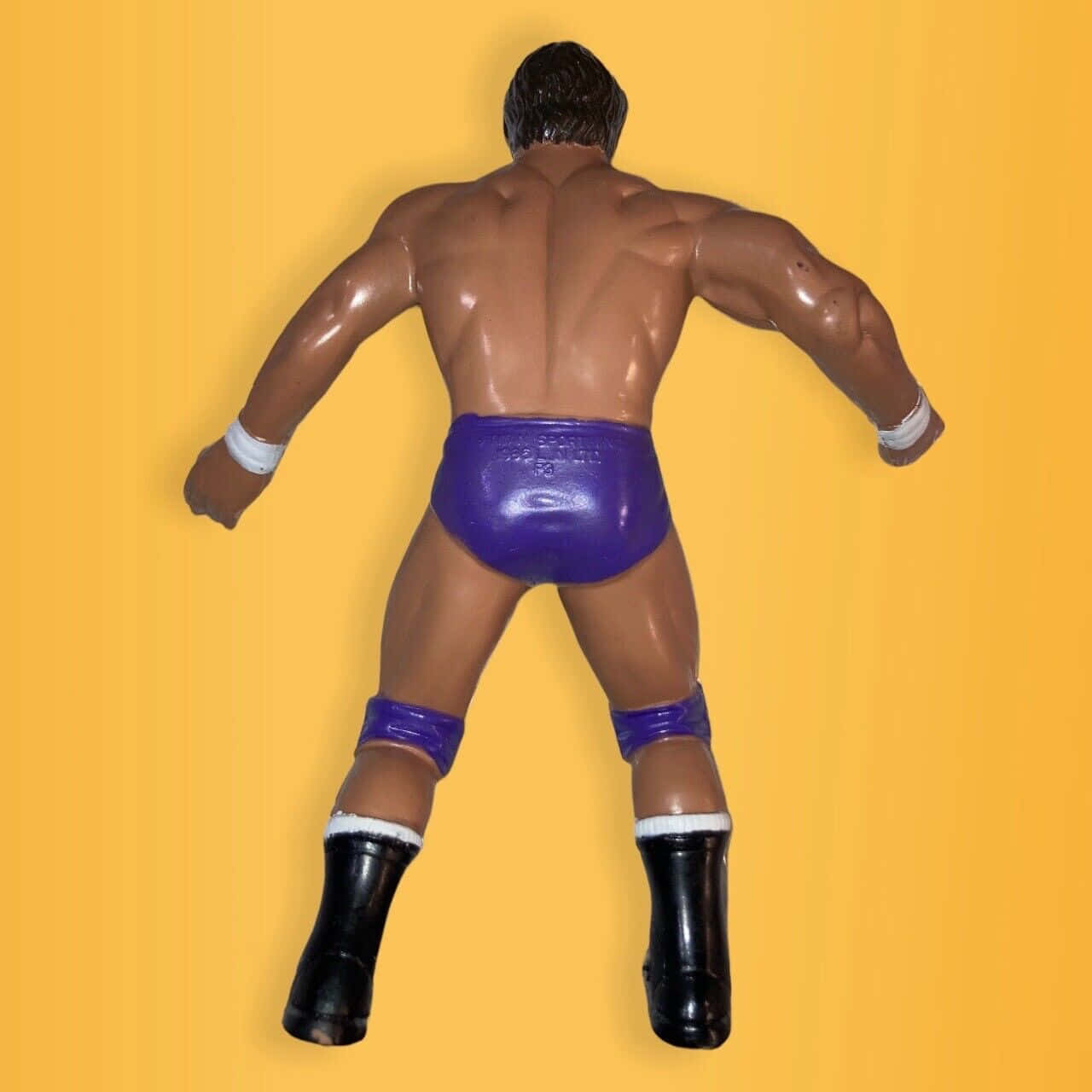 Tito Santana 行動人偶背面視圖 壁紙 — 一個肌肉發達的摔角動作人偶，從背後看，背景為純黃色。