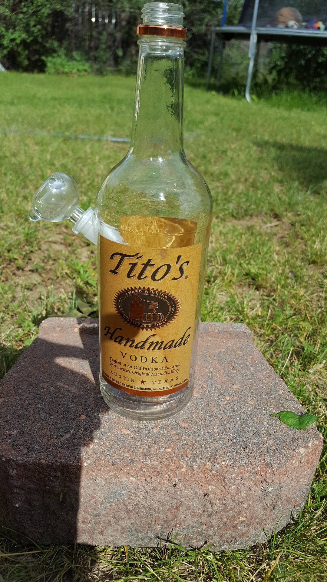 Tito's伏特加酒瓶與水煙槍配件，放在草地上的磚上。