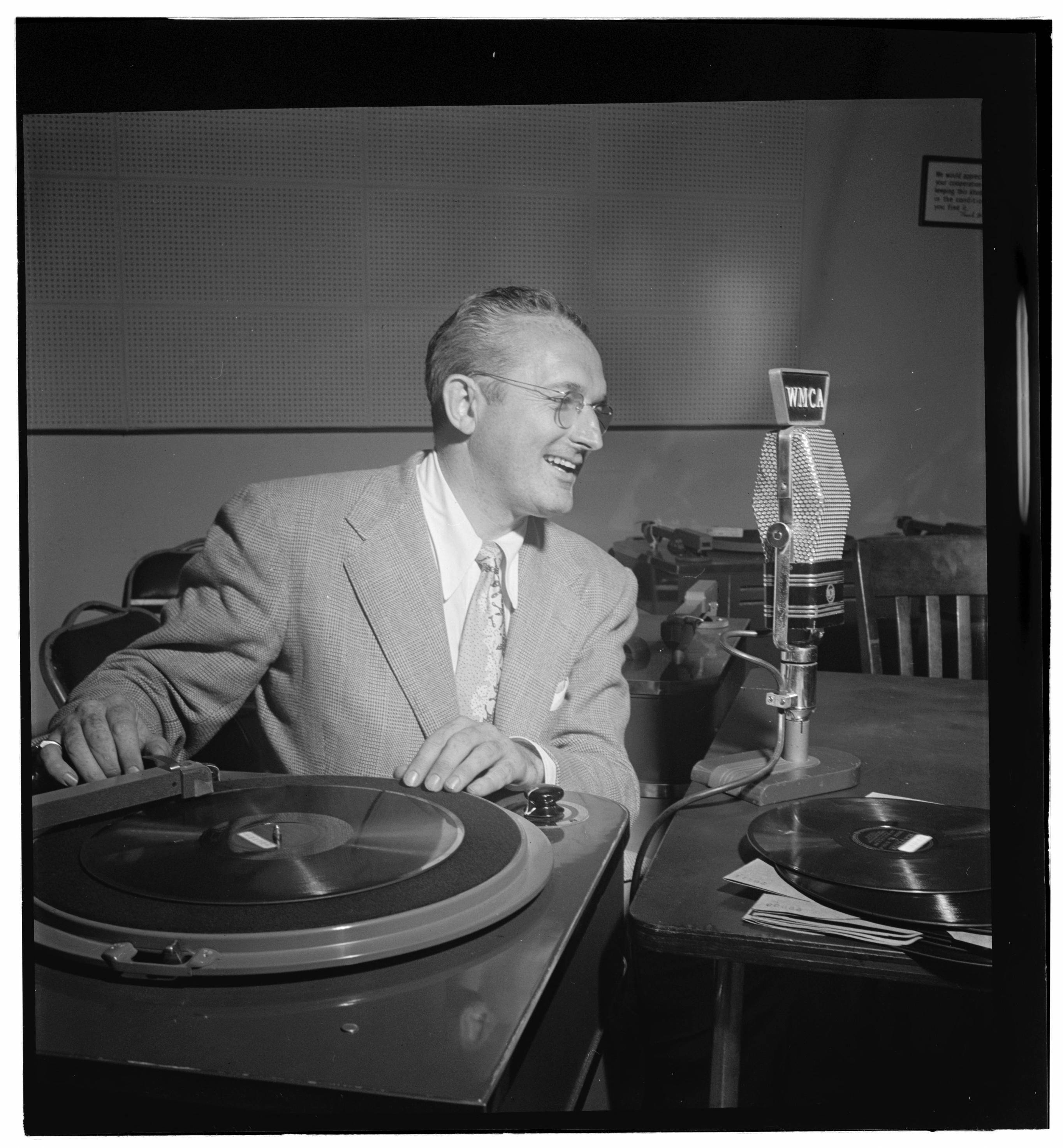 Tommy Dorsey 當電台主持人照片 壁紙 — 一位身穿西裝、戴眼鏡的 smiling 男士在收音機錄音室裡，在復古麥克風旁邊用唱盤播放黑膠唱片。
