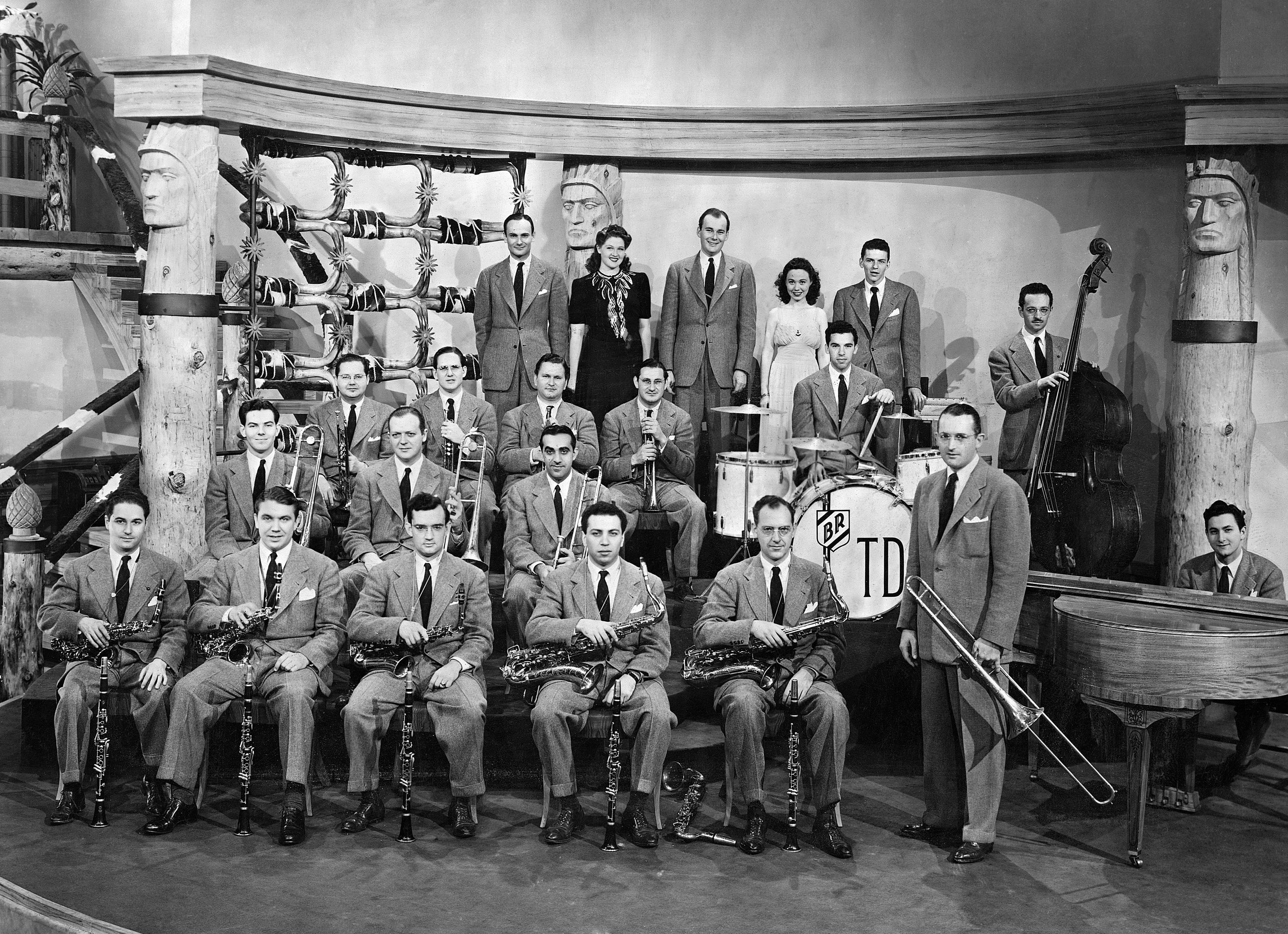 Tommy Dorsey 與他的樂團合照 壁紙 — 一張復古黑白照片，爵士樂隊在帶有部落主題裝飾和樂器的舞台上擺姿勢。