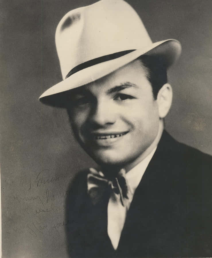 Tony Canzoneri 肖像照 壁紙 — 一位微笑的男子戴著軟呢帽和西裝，在左側有手寫簽名的復古工作室肖像中擺姿勢。
