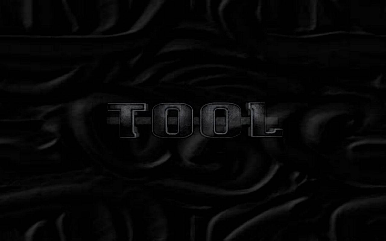 美國硬搖滾樂團Tool的經典形象 壁紙 — 「TOOL」一詞在黑暗、漣漪般的黑色布料背景上以金屬字母微弱發光。