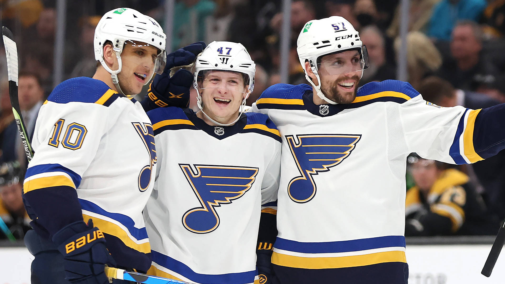 Torey Krug 與 Brayden Schenn 及 David Perron 同慶 壁紙 — 三名身穿白色球衣的聖路易斯藍調冰球球員在冰上熱情慶祝，笑容燦爛，互相搭肩。