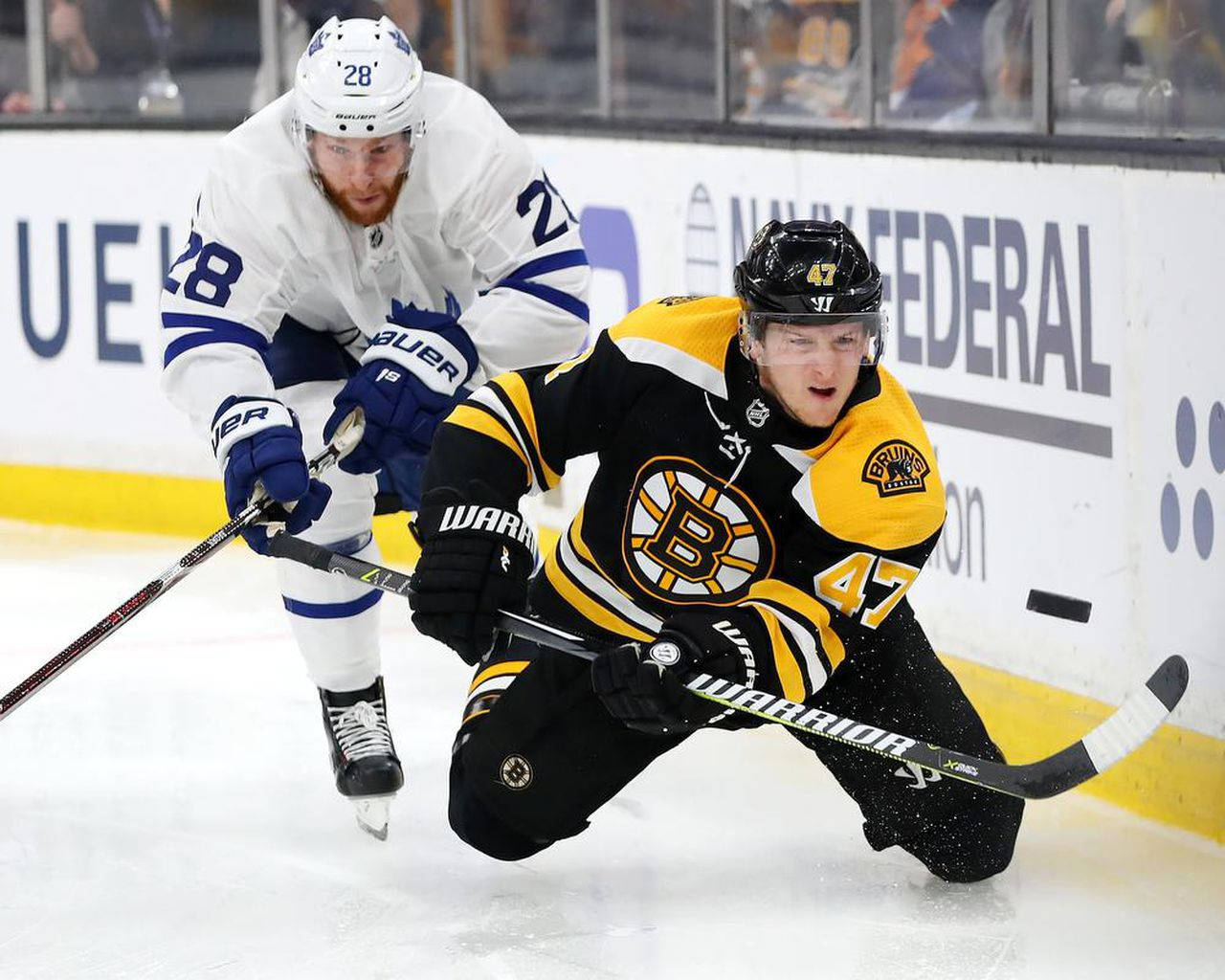 Torey Krug 與 Connor Brown（2019） 壁紙 — 兩名曲棍球運動員在冰上激烈對抗，一人身穿黑黃色球衣，另一人身穿白藍色球衣，雙方都專注於控球。