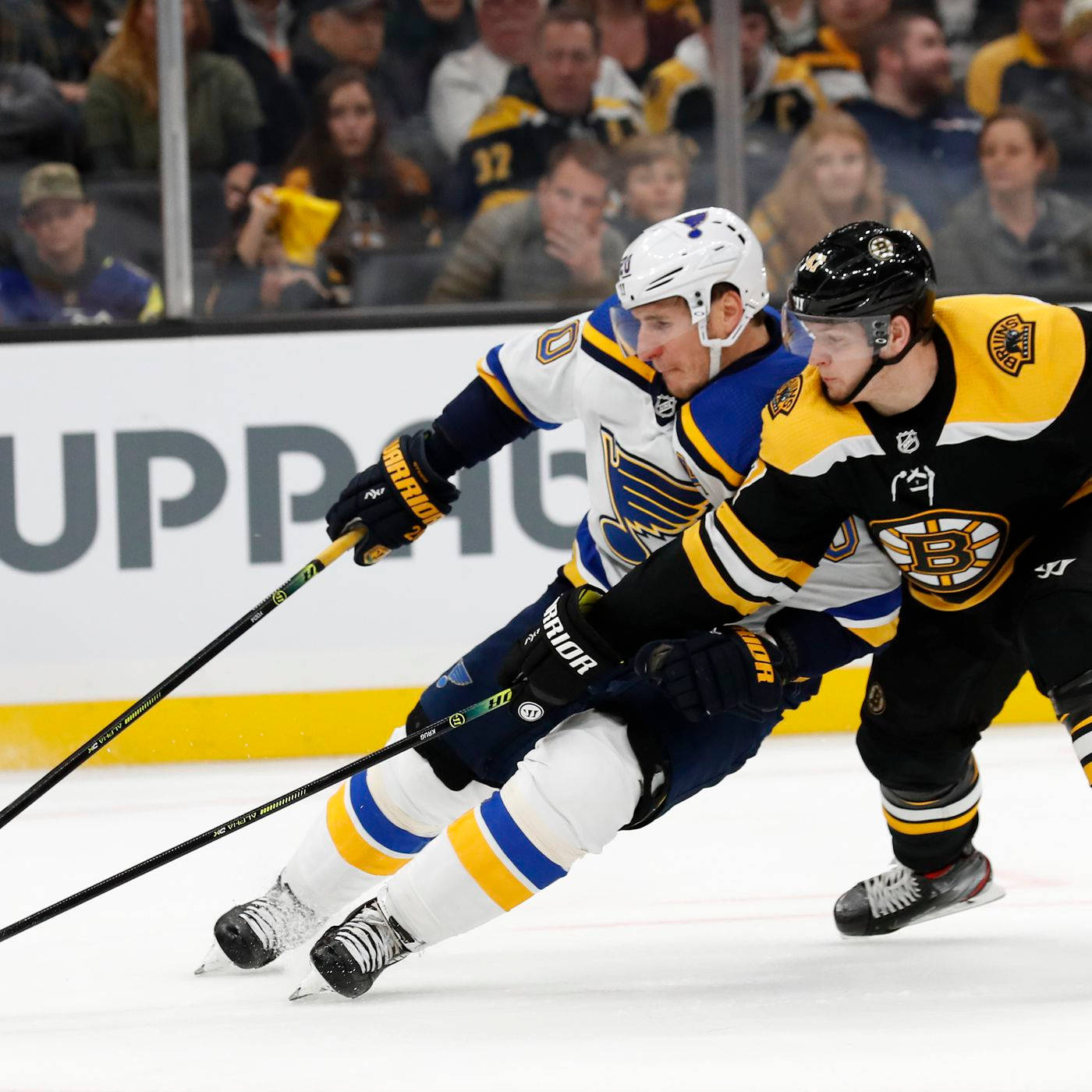 Torey Krug 試圖奪球 壁紙 — 兩名冰球運動員在冰上激烈爭奪控球權，觀眾在玻璃後面觀看。