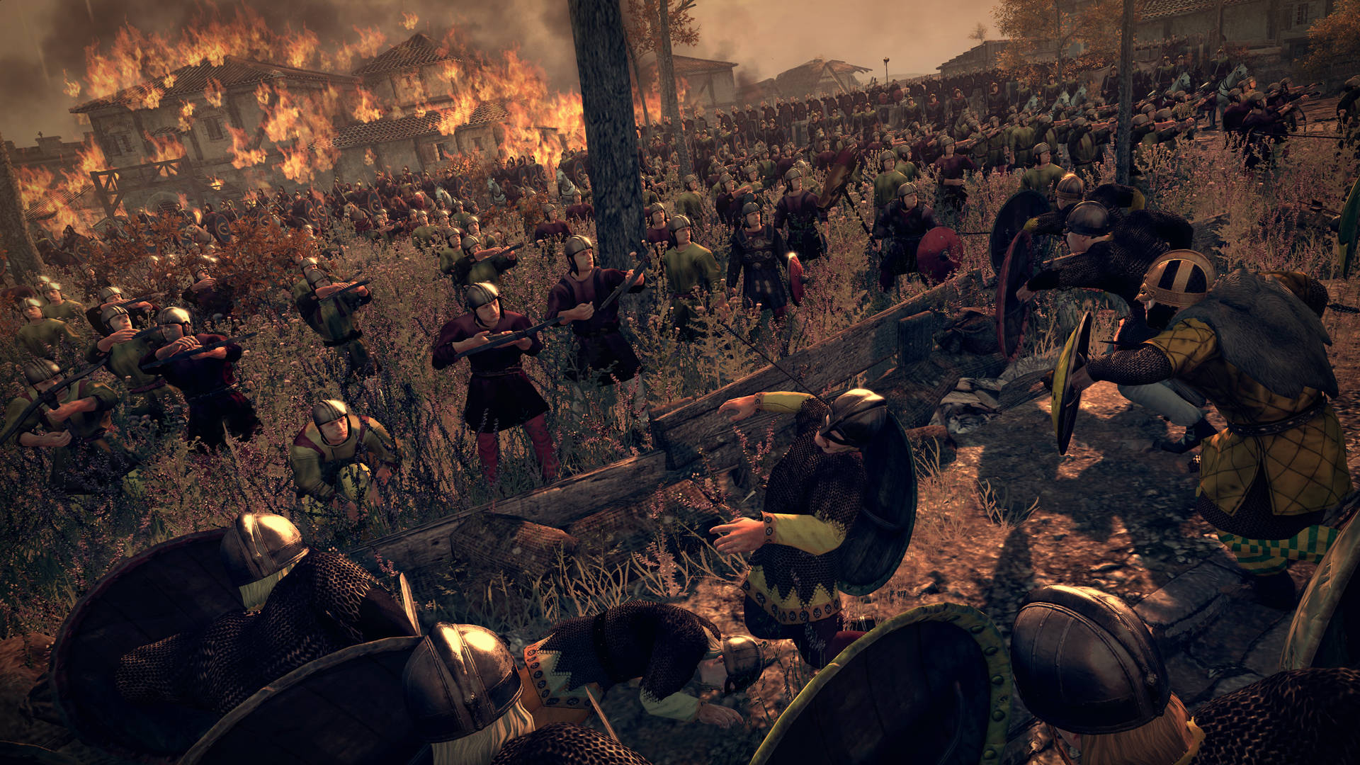 Total War: Attila 田野伏擊 壁紙 — 一個混亂的中世紀戰場，身穿盔甲的戰士在燃燒的木結構和煙霧中交戰。