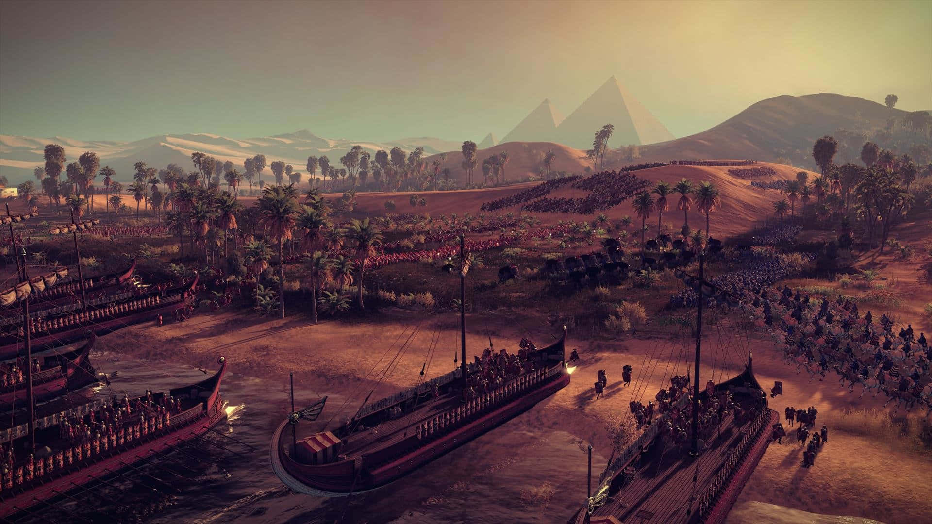 《Total War：羅馬2》最佳陣營戰場背景：紅沙黃天 壁紙 — 古埃及戰艦停泊在金字塔附近，軍隊在黃金時刻的沙漠景觀中行進。
