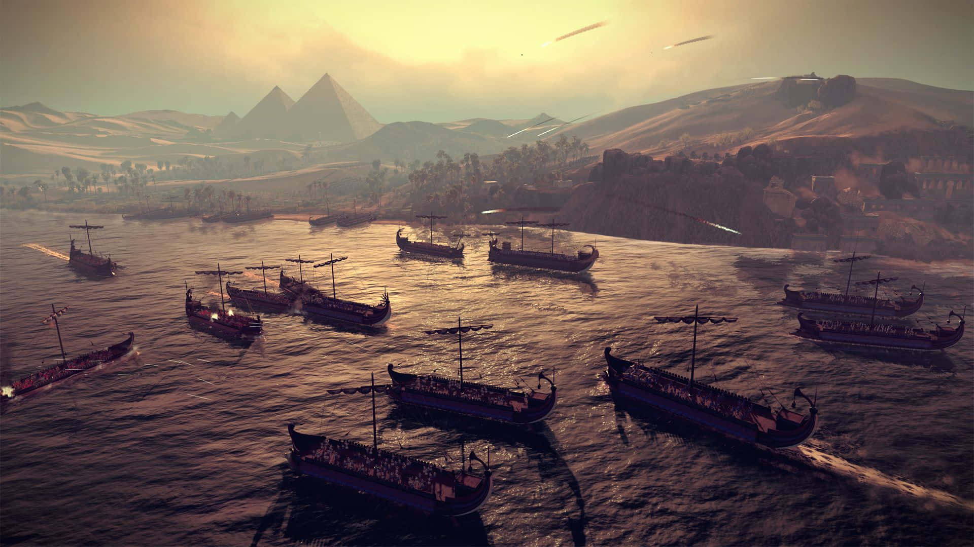 《Total War：羅馬2》經典戰場場景 壁紙 — 一支古代戰艦艦隊在金色河流上航行，沙漠遠處的金字塔在日落時分升起。