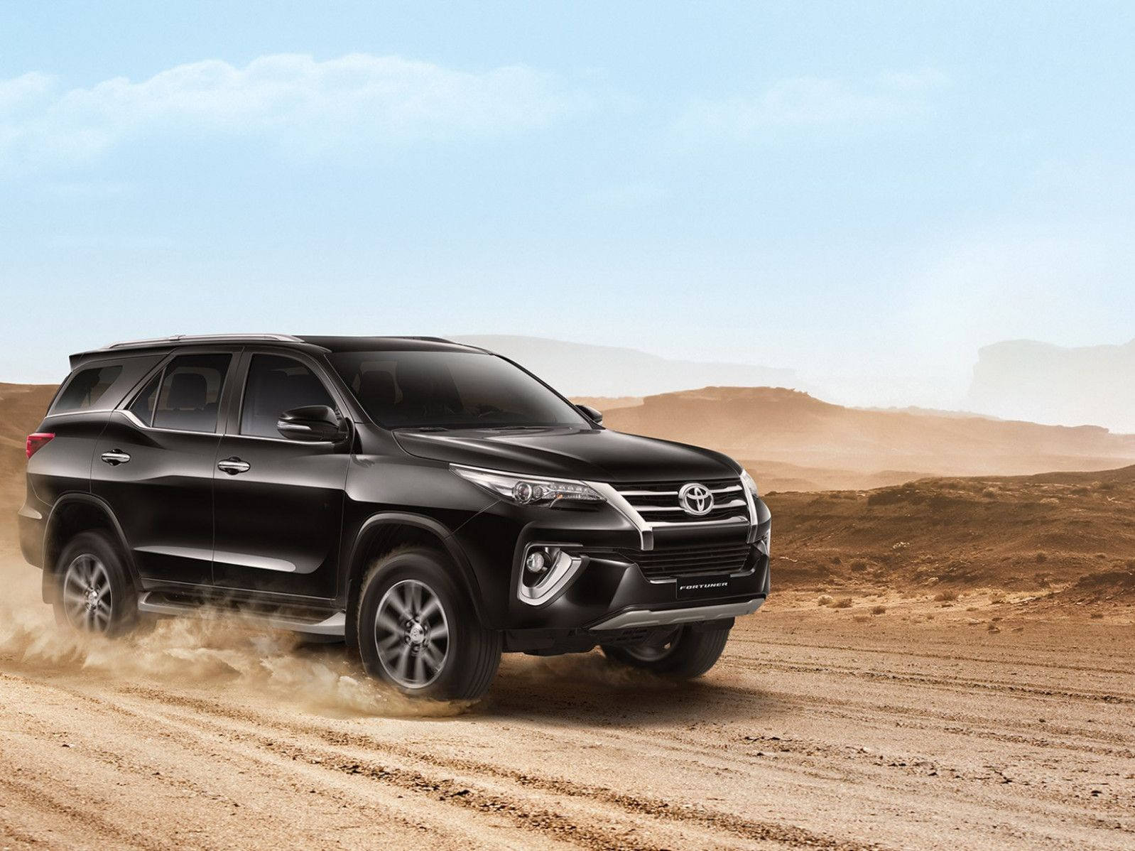 黑色豐田 Fortuner SUV 在沙漠地形上行駛，揚起沙塵。