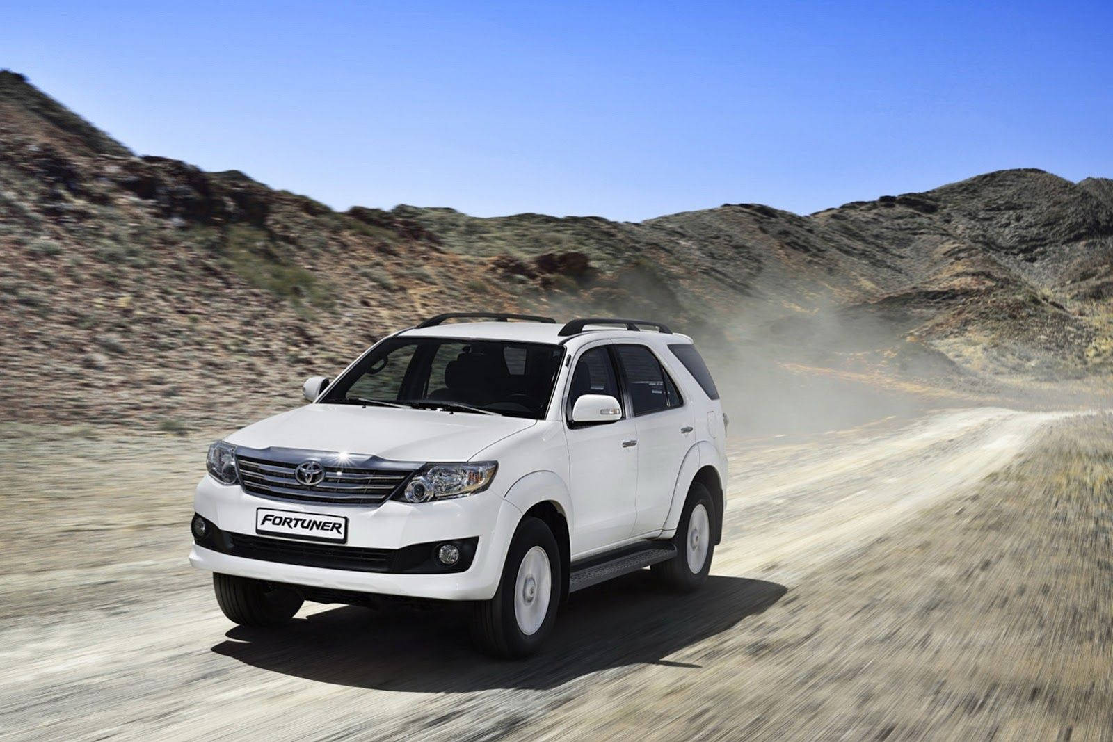 白色豐田 Fortuner SUV 在沙漠景觀中的泥路上快速行駛。