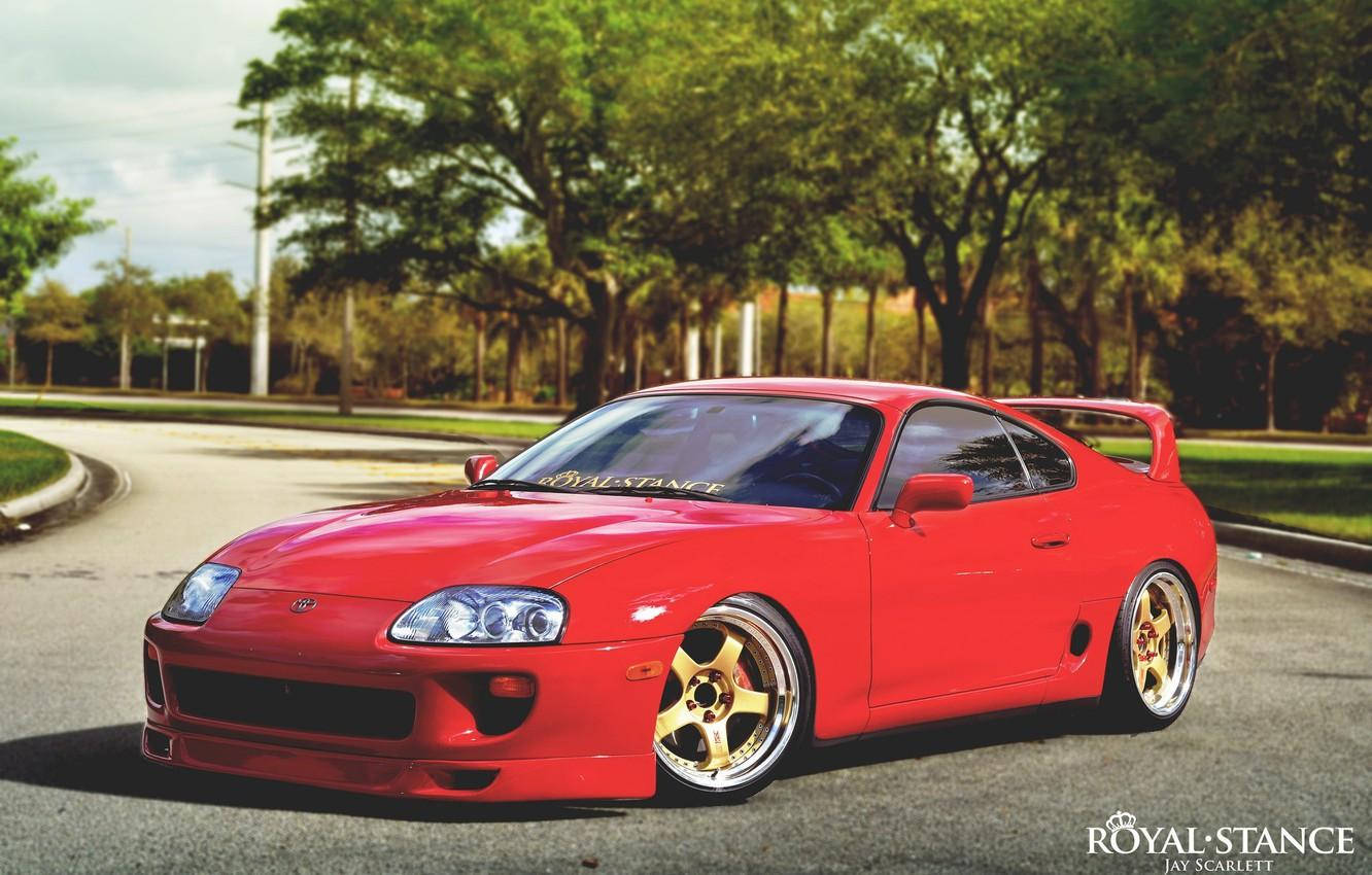 自然吸氣紅色 Toyota Supra Mk4 壁紙 — 一輛鮮紅色的豐田Supra配金色輪圈，在明亮的日光下，於綠樹成蔭的道路上優雅地轉彎。
