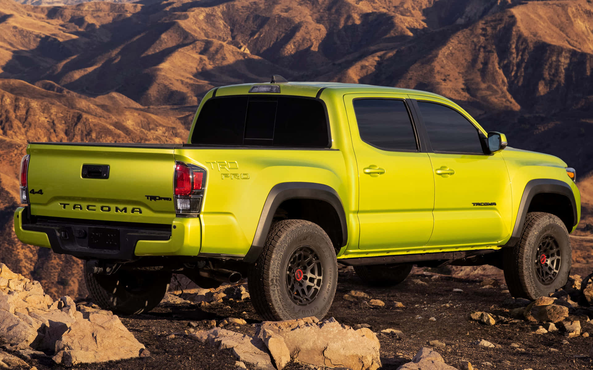 全地形 Toyota TRD 越野車 壁紙 — 一輛充滿活力的青檸綠色豐田 Tacoma TRD Pro 皮卡車停在岩石地形上，背景是陽光照耀的沙漠山脈。