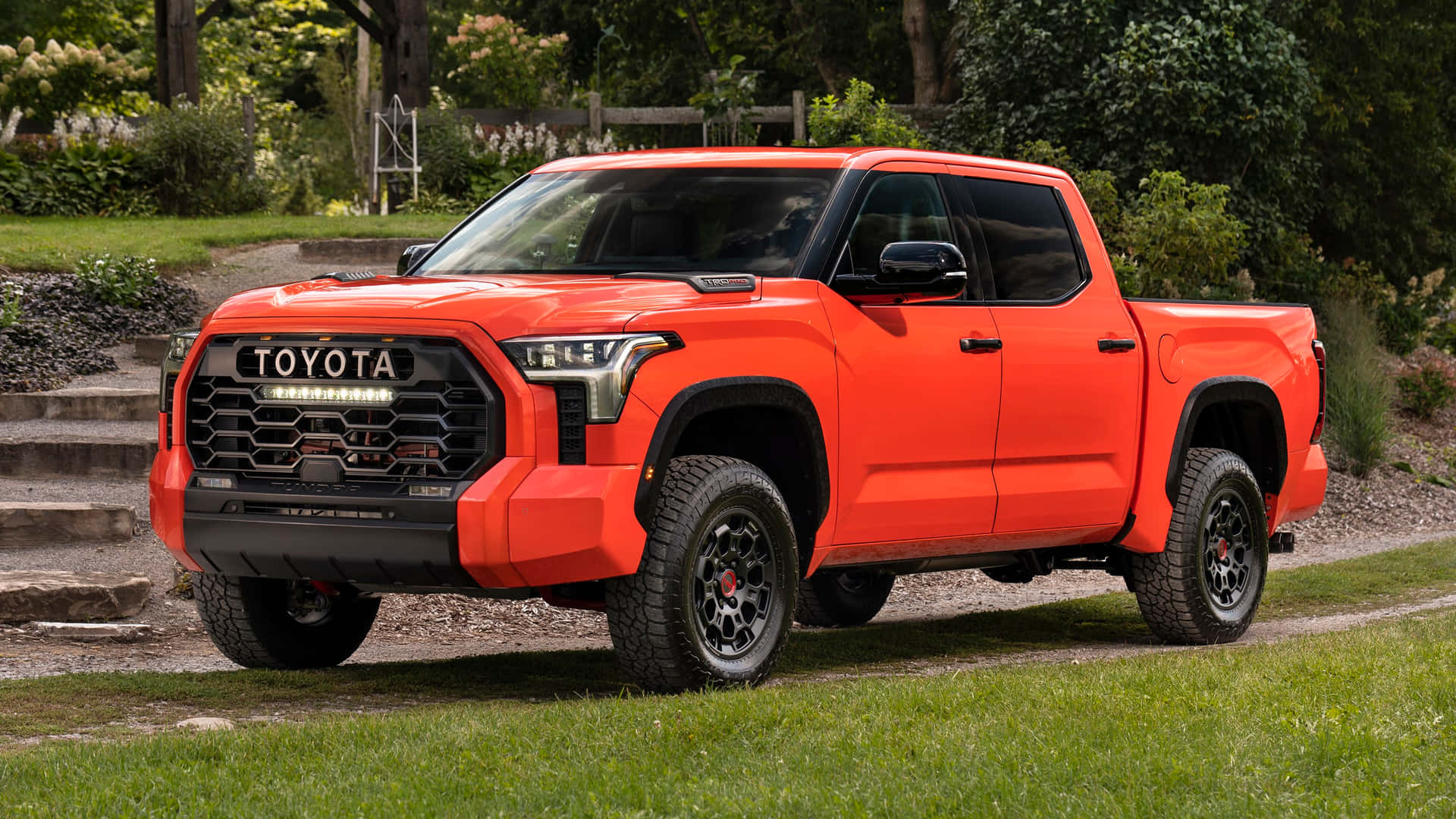 亮橙色豐田 Tacoma 皮卡車停在石階附近的草地上。
