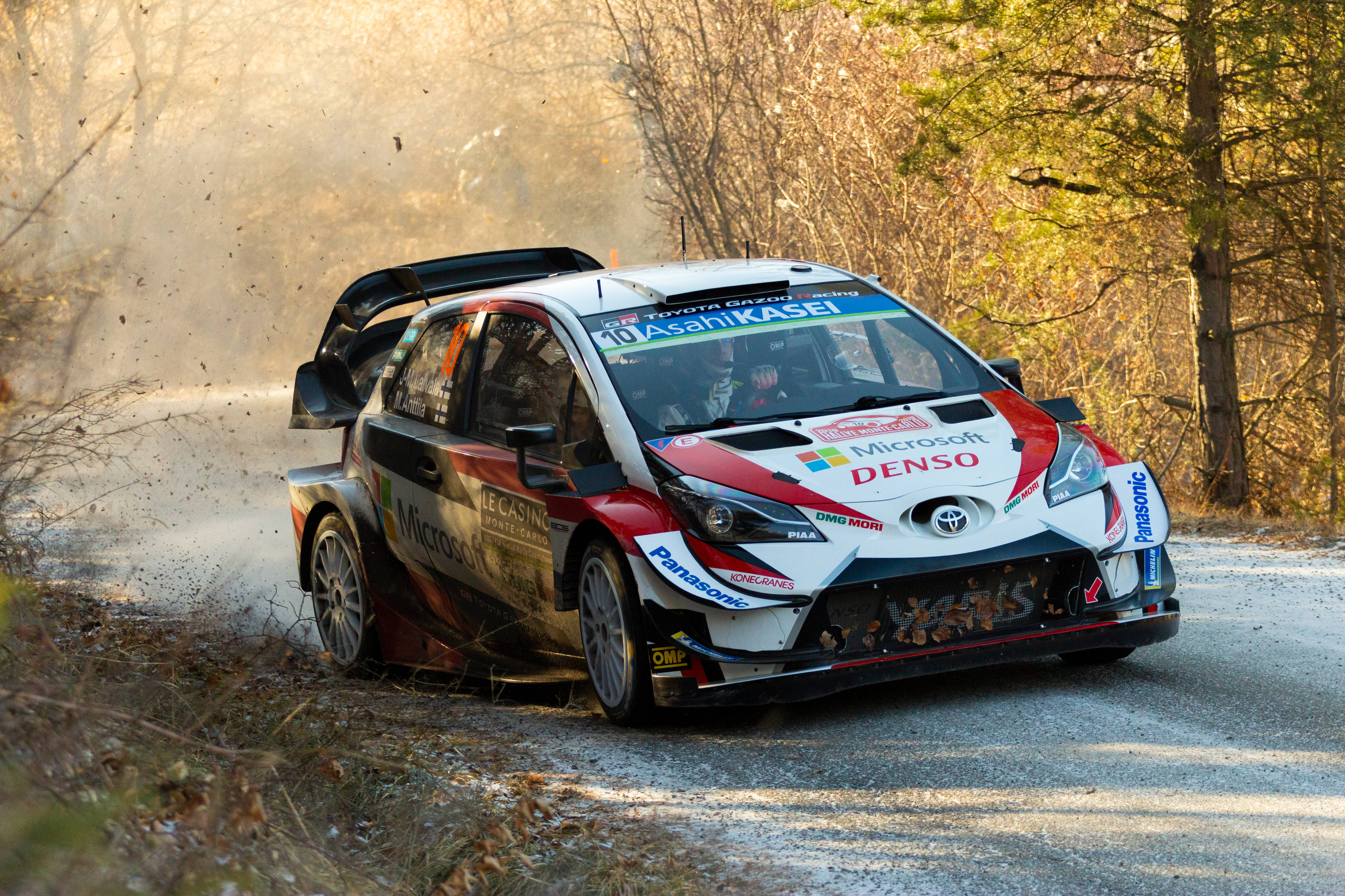 Toyota Yaris 越野賽車賽道挑戰 壁紙 — 一輛紅白黑色的豐田拉力賽車在陽光照耀的林間道路上疾馳，揚起灰塵。