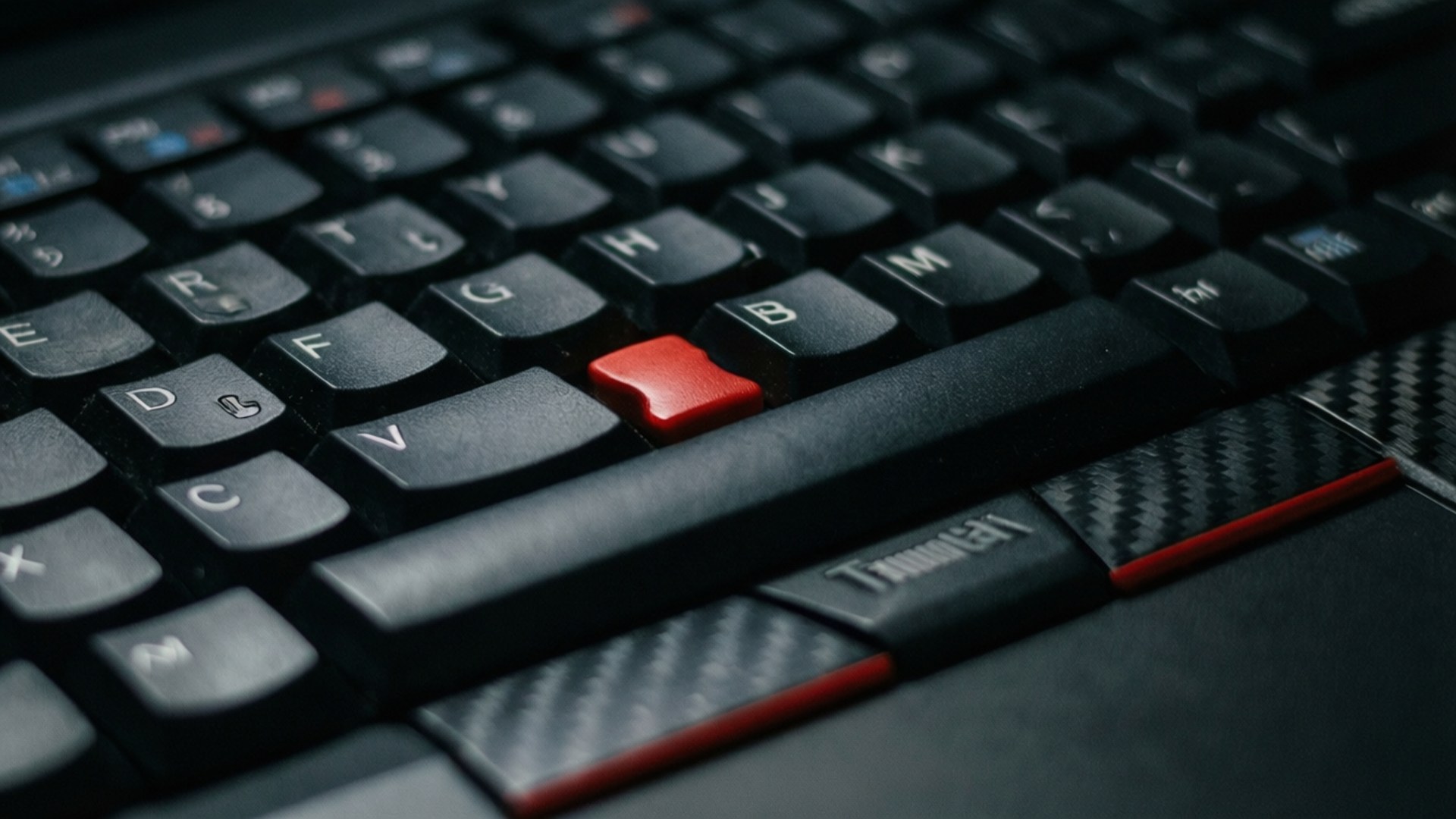 TrackPoint 微距特寫 壁紙 — 黑色手提電腦鍵盤特寫，帶有紅色TrackPoint和碳纖維裝飾，在柔和燈光下。
