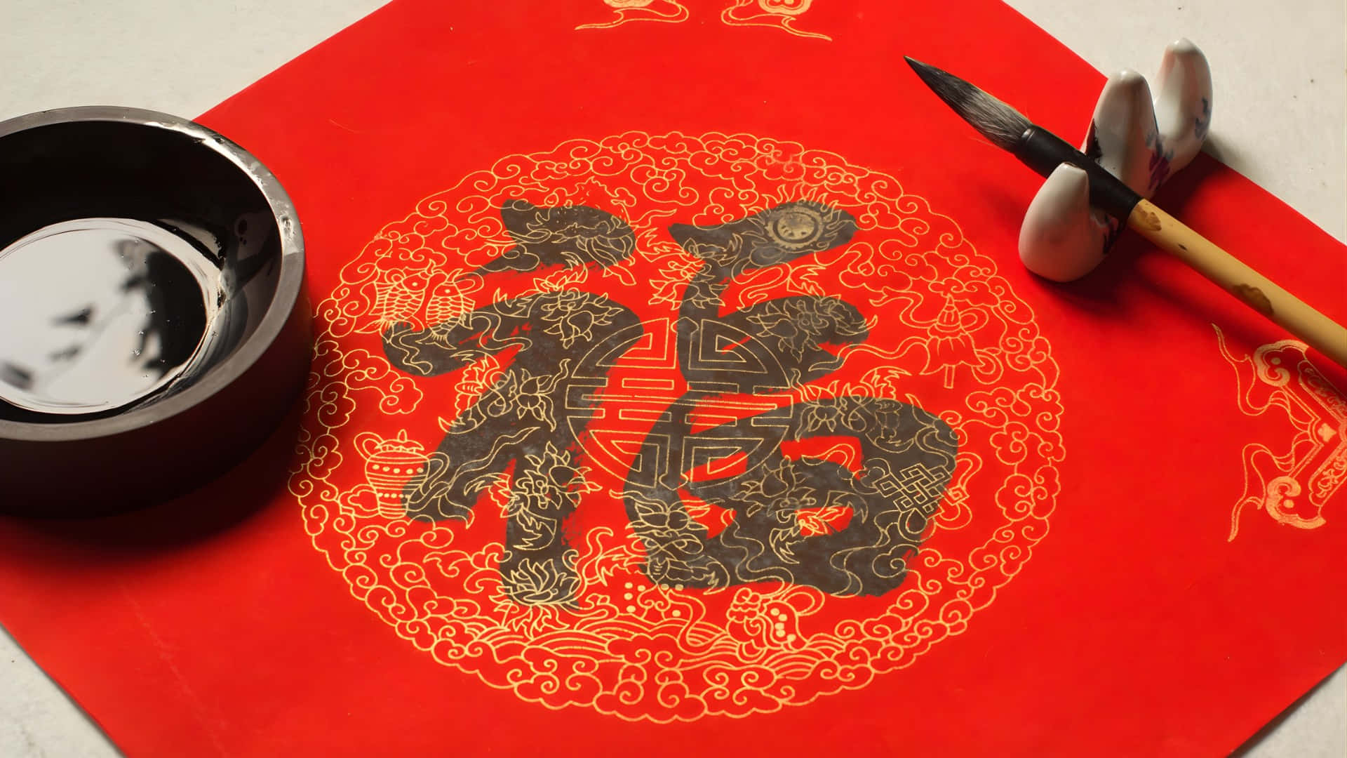  壁紙 — 傳統中國書法設置，紅色紙上有一個粗體黑色「福」字，周圍環繞著精緻的金色圖案，並配有硯台和毛筆。