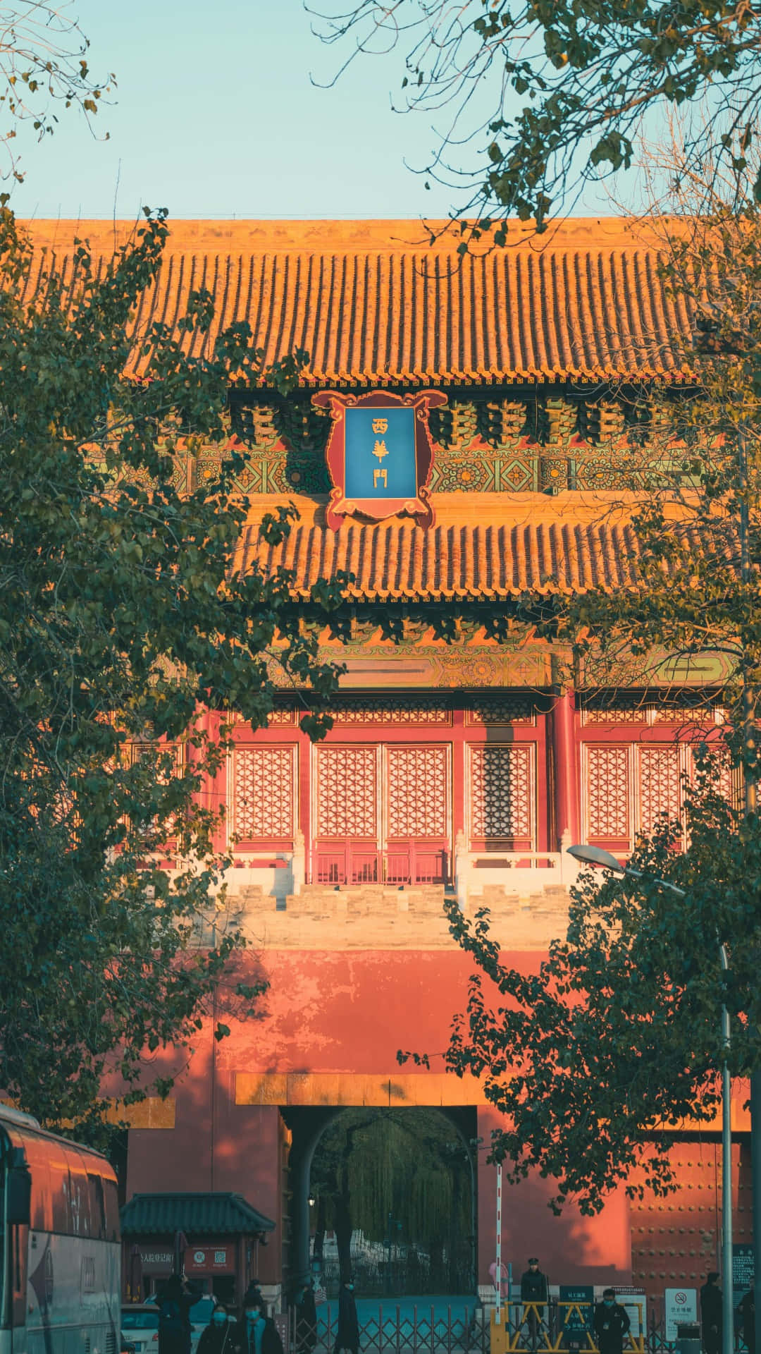  壁紙 — 一座傳統中式門樓，紅牆金瓦，沐浴在溫暖的夕陽光中，四周綠樹環繞。
