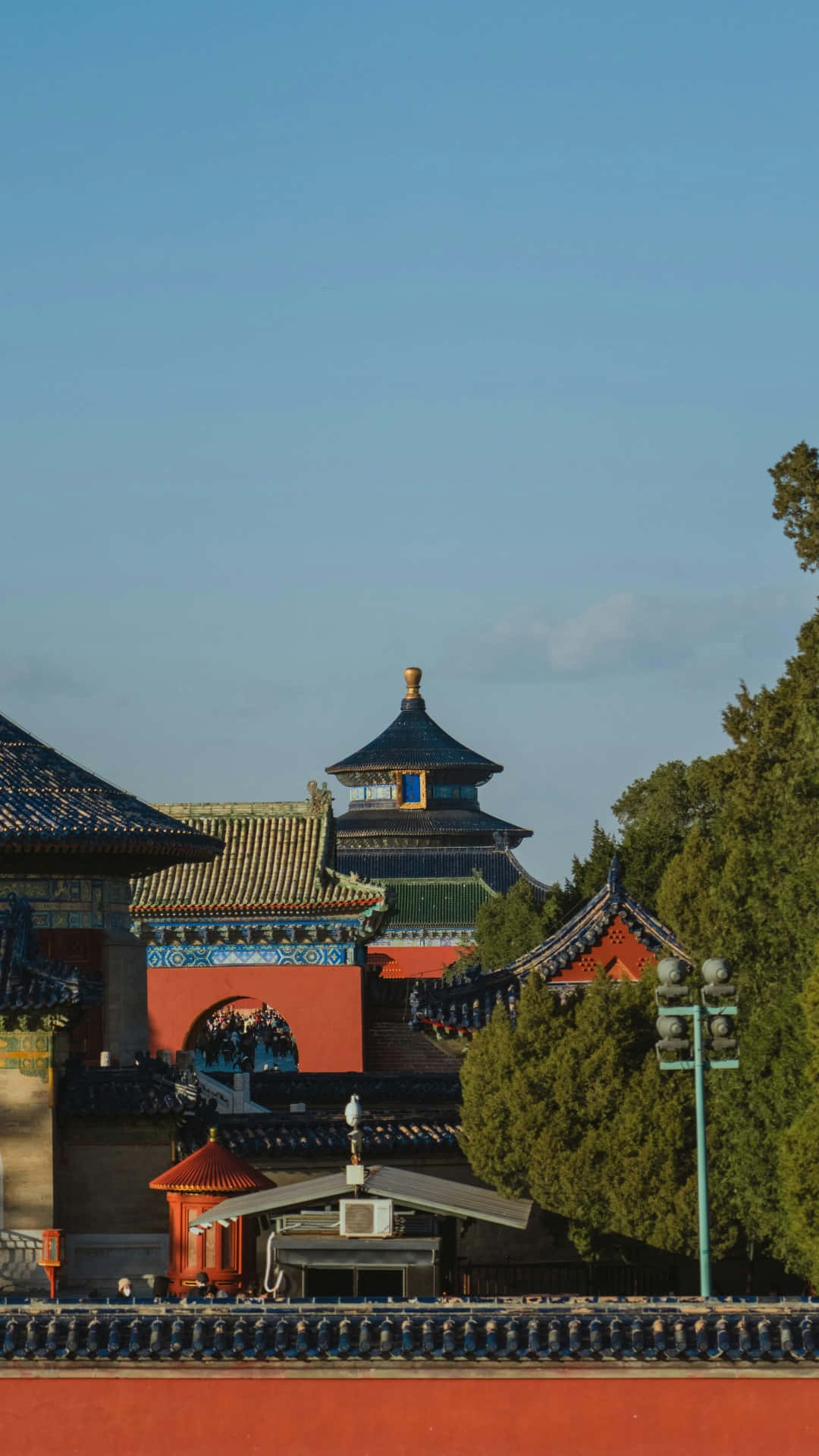  壁紙 — 傳統中國寺廟屋頂，飾有華麗藍色瓦片和紅色牆壁，在清澈藍天下被茂密綠樹環繞。