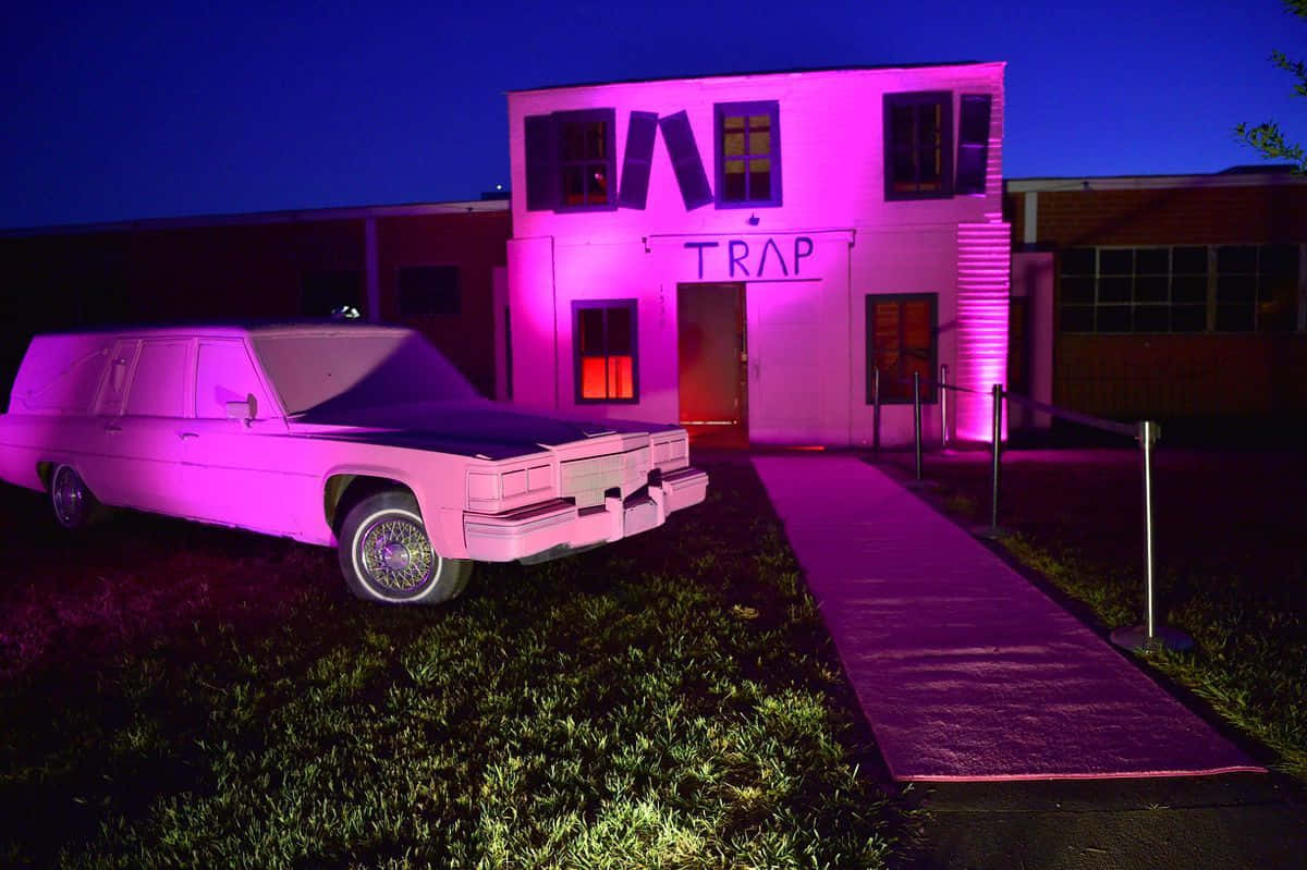 粉紅燈光照亮的靈車停在標有 trap 的建築物前，在夜間。