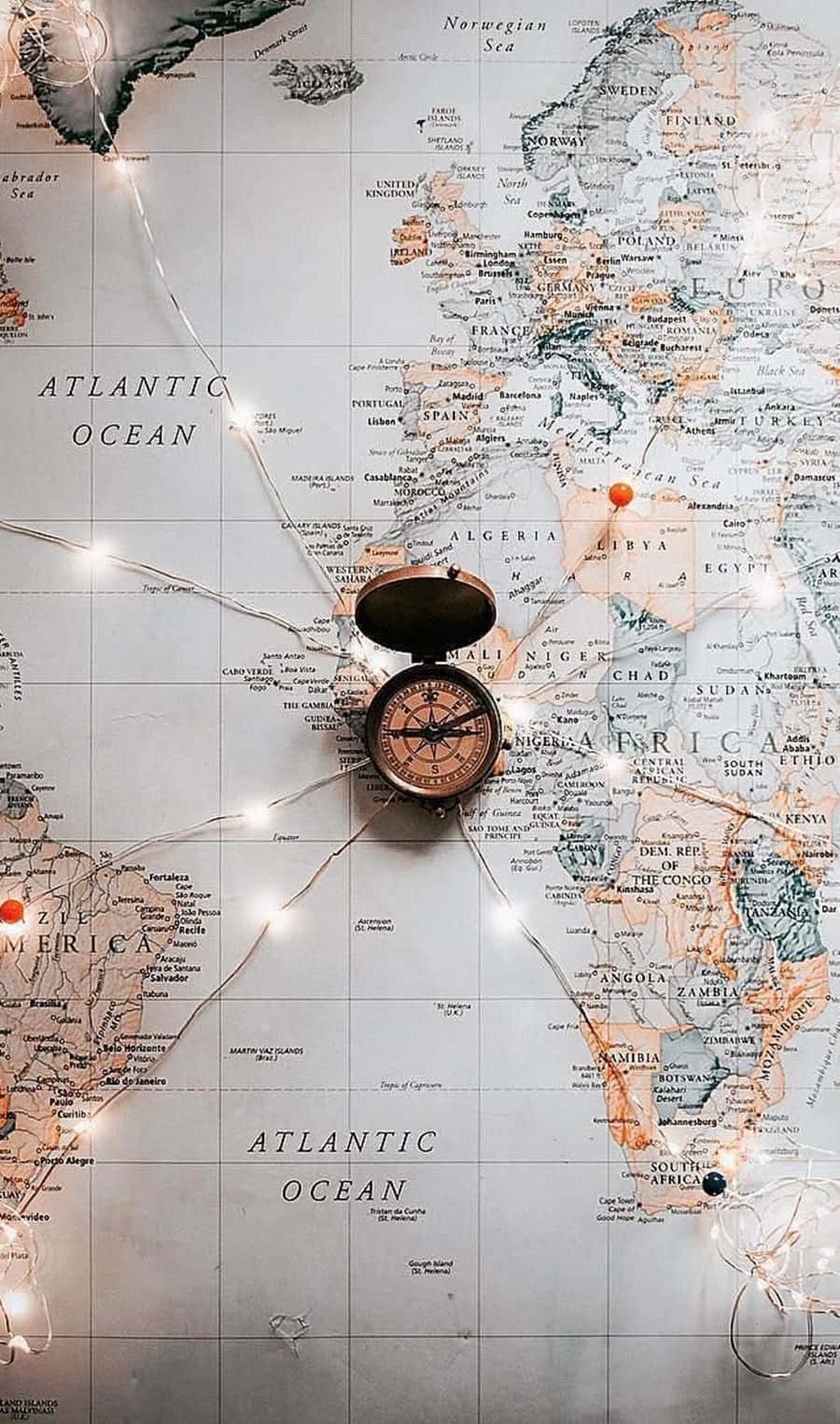 Travel Aesthetic Phone Compass 壁紙 — 一個復古指南針放在一個由精緻燈串照亮、散發溫暖光芒的世界地圖上。