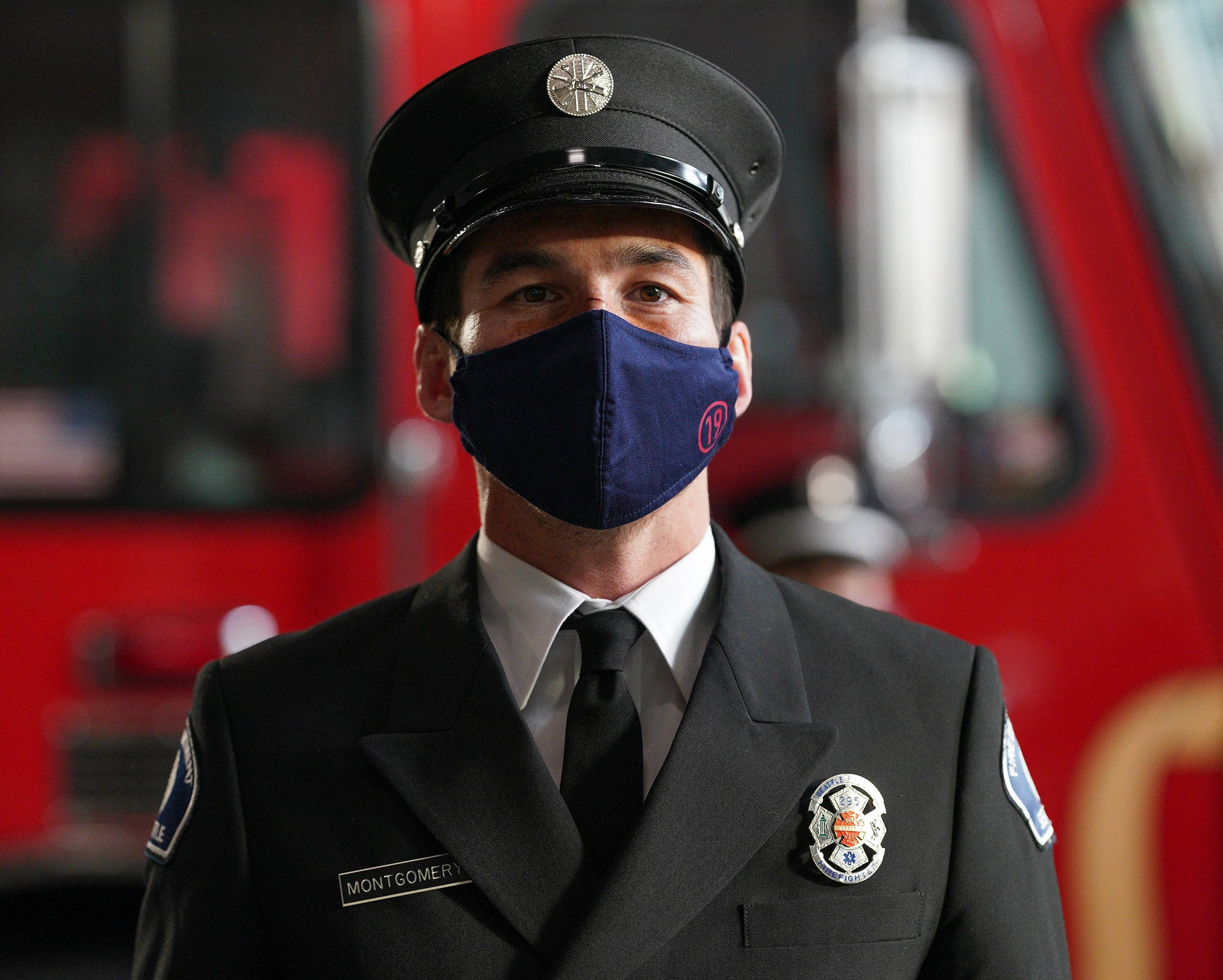 Travis Montgomery 在《Station 19》中的精彩表現 壁紙 — 一名穿著制服和口罩的消防員，眼神專注，自信地站在紅色消防車前。