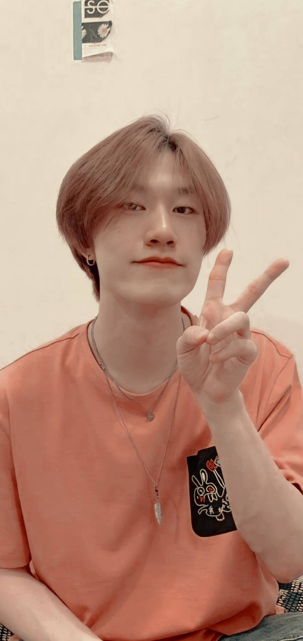 Treasure 主唱 Yedam 壁紙 — 一位淺棕色頭髮的年輕男子在溫暖燈光的室內環境中微笑著做出和平手勢。