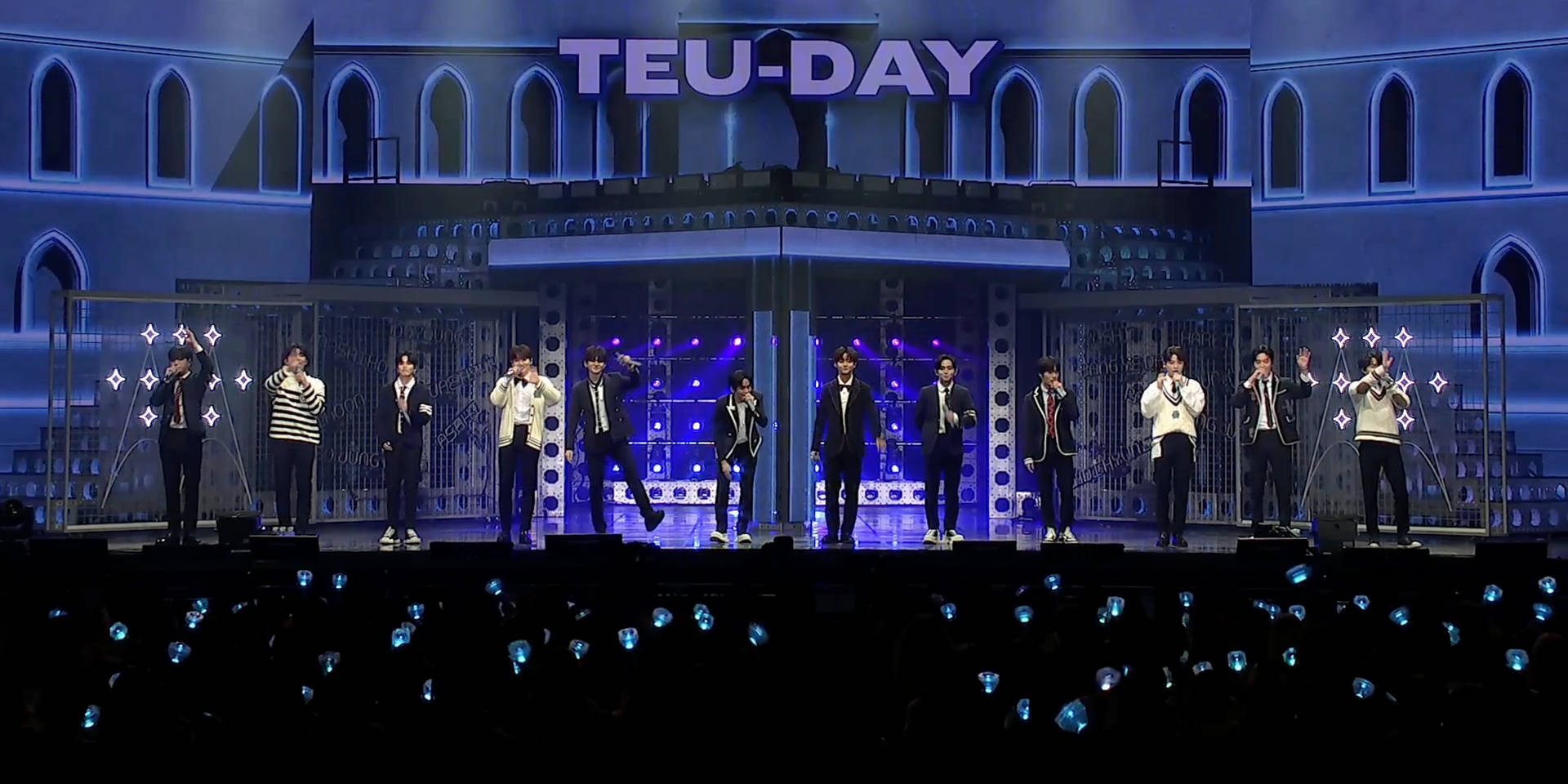 K-pop組合在藍色燈光舞台上表演，粉絲們舉著發光的燈光。