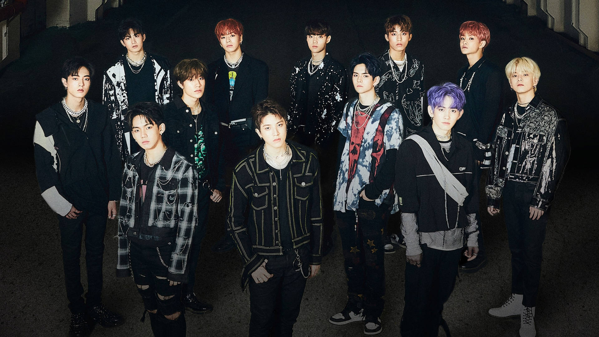 K-pop 團體在黑暗的城市小巷中擺姿勢，擁有色彩繽紛的頭髮和時尚服裝。