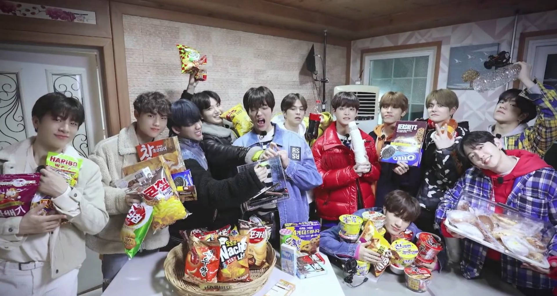 K-pop 團體在熱鬧的室內環境中拿著零食和食物。