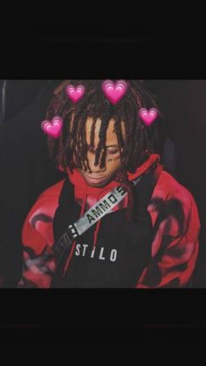 Trippie Redd 周圍飄心形 壁紙 — 一個梳著辮子的人穿著紅色和黑色的連帽衫，心形在頭頂漂浮，背景為深色。