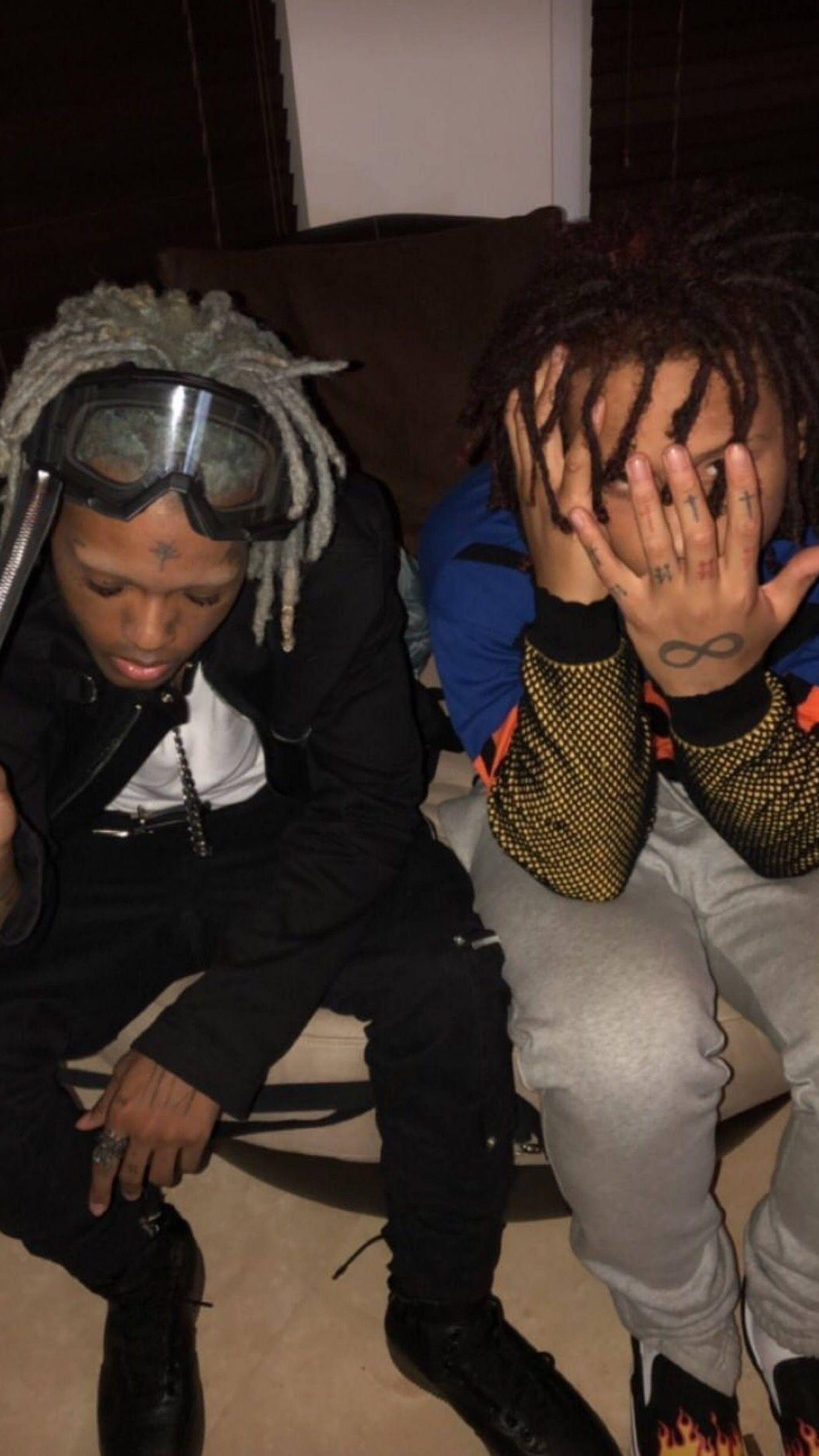 Trippie Redd 手部紋身 壁紙 — 兩名年輕男子留著辮子頭坐在沙發上，一人戴著護目鏡，另一人用手遮臉，紋身可見。