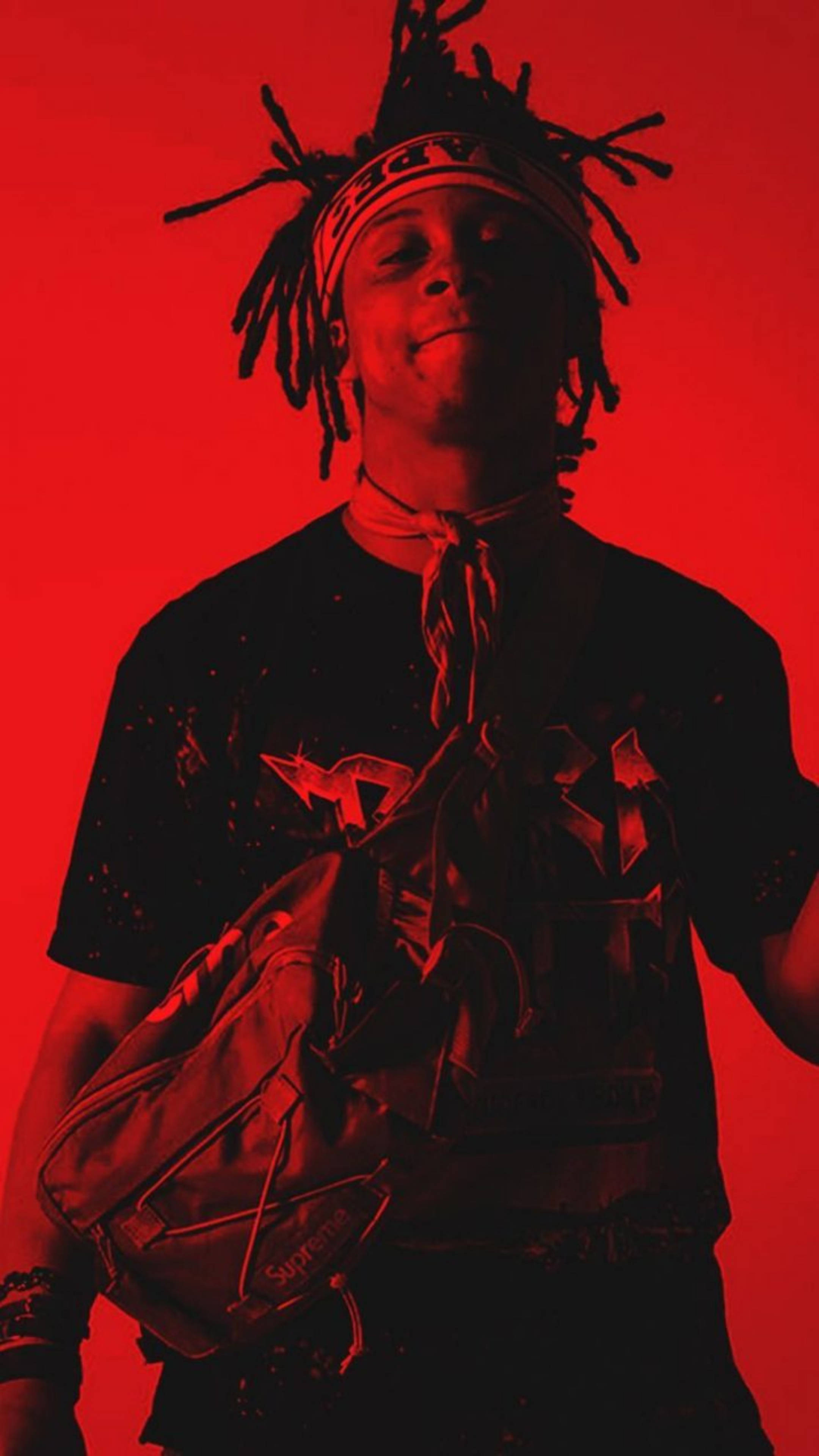 Trippie Redd 照片拍攝 壁紙 — 一位年輕男子留著辮子頭、戴著頭帶，在純紅色背景前自信微笑，身穿圖案T恤並背著背包。