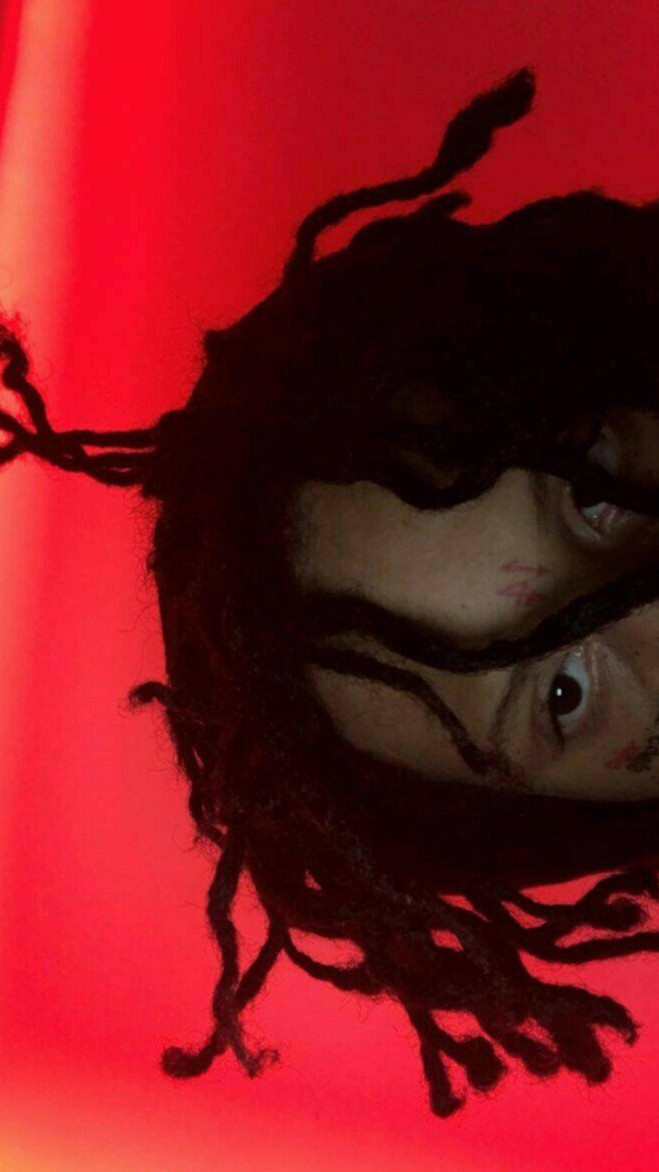 Trippie Redd 編髮特寫 壁紙 — 一個有深色辮子和可見紋身的人，在鮮紅色背景下強烈凝視。