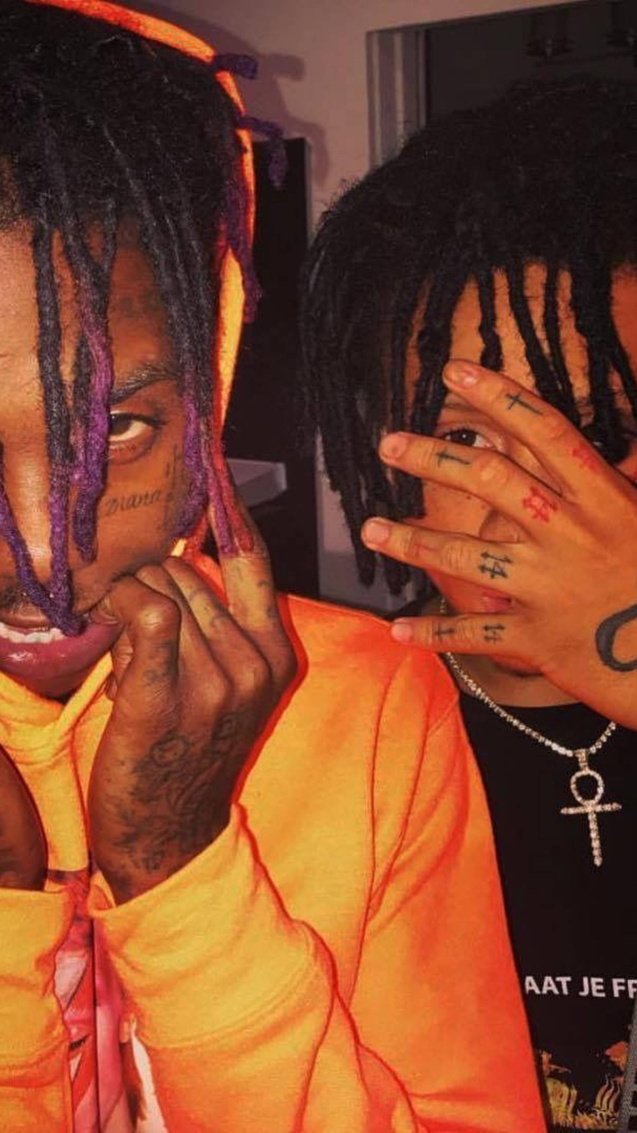 Trippie Redd 與 Famous Dex 壁紙 — 兩個有辮子頭和紋身的人緊密地擺姿勢，其中一個用手遮住臉，兩人都穿著鮮豔的橙色衣服在室內。
