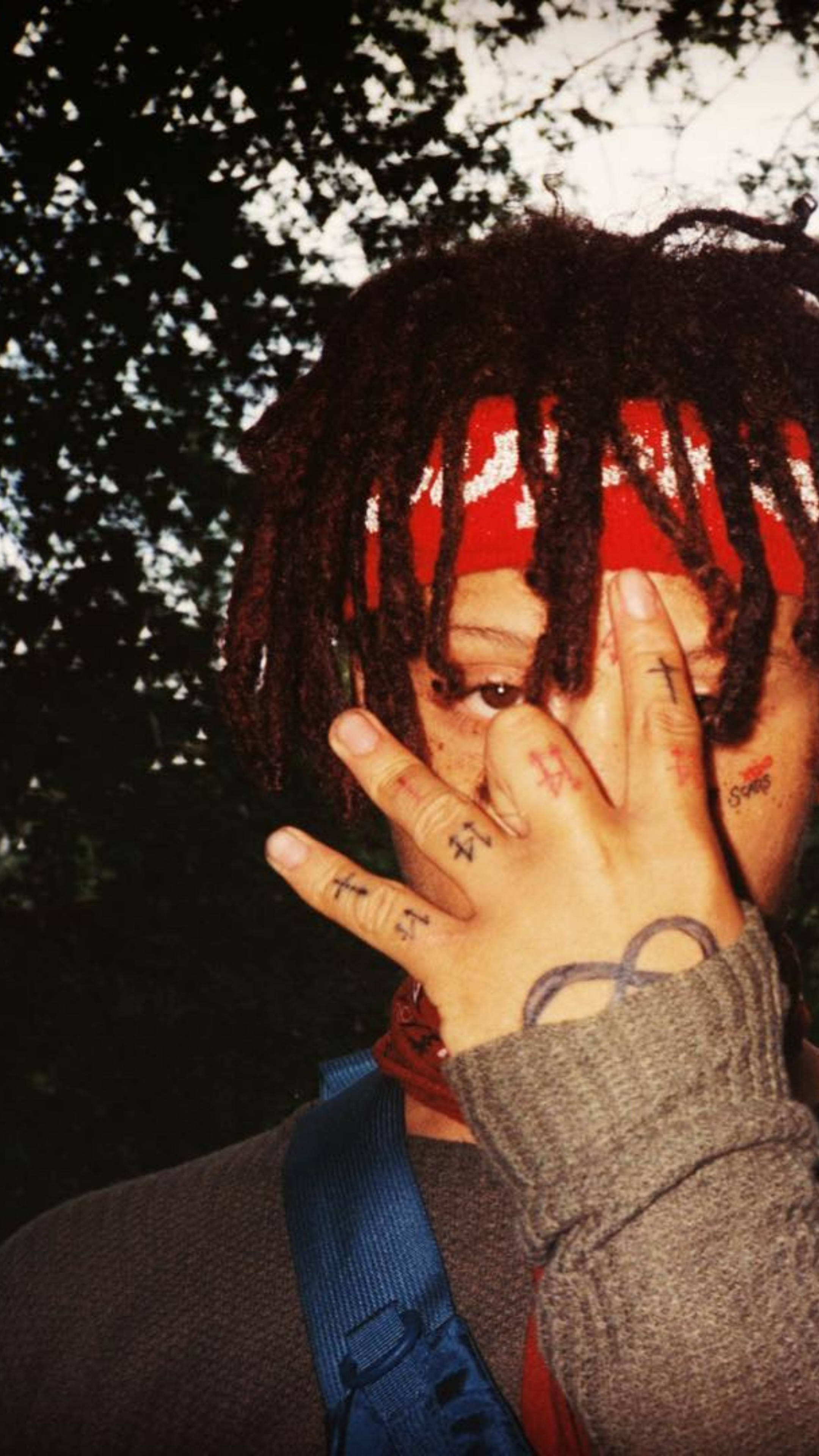 Trippie Redd 閃光攝影 壁紙 — 一個有辮子頭和紅色頭巾的人，用一隻佈滿紋身和符號的手部分遮住臉。