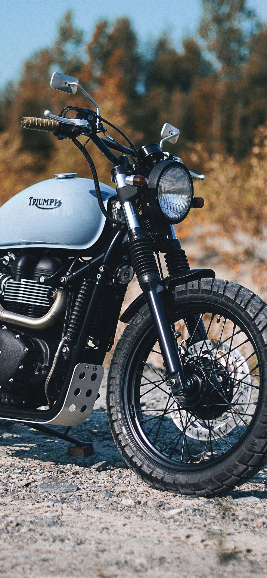 復古Triumph電單車停在碎石上，後面有秋天的樹木。