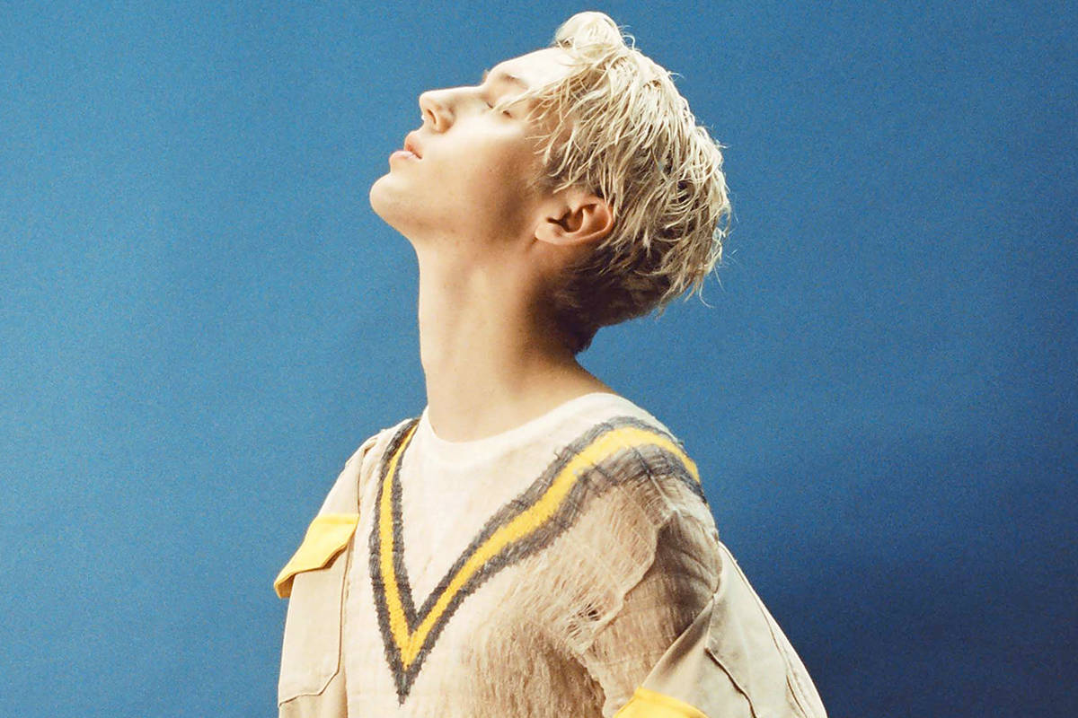 Troye Sivan 澳洲流行天王 壁紙 — 一個年輕人有著蓬鬆的金髮，頭向後靠在純藍色工作室背景上，閉著眼睛，陷入寧靜的沉思。