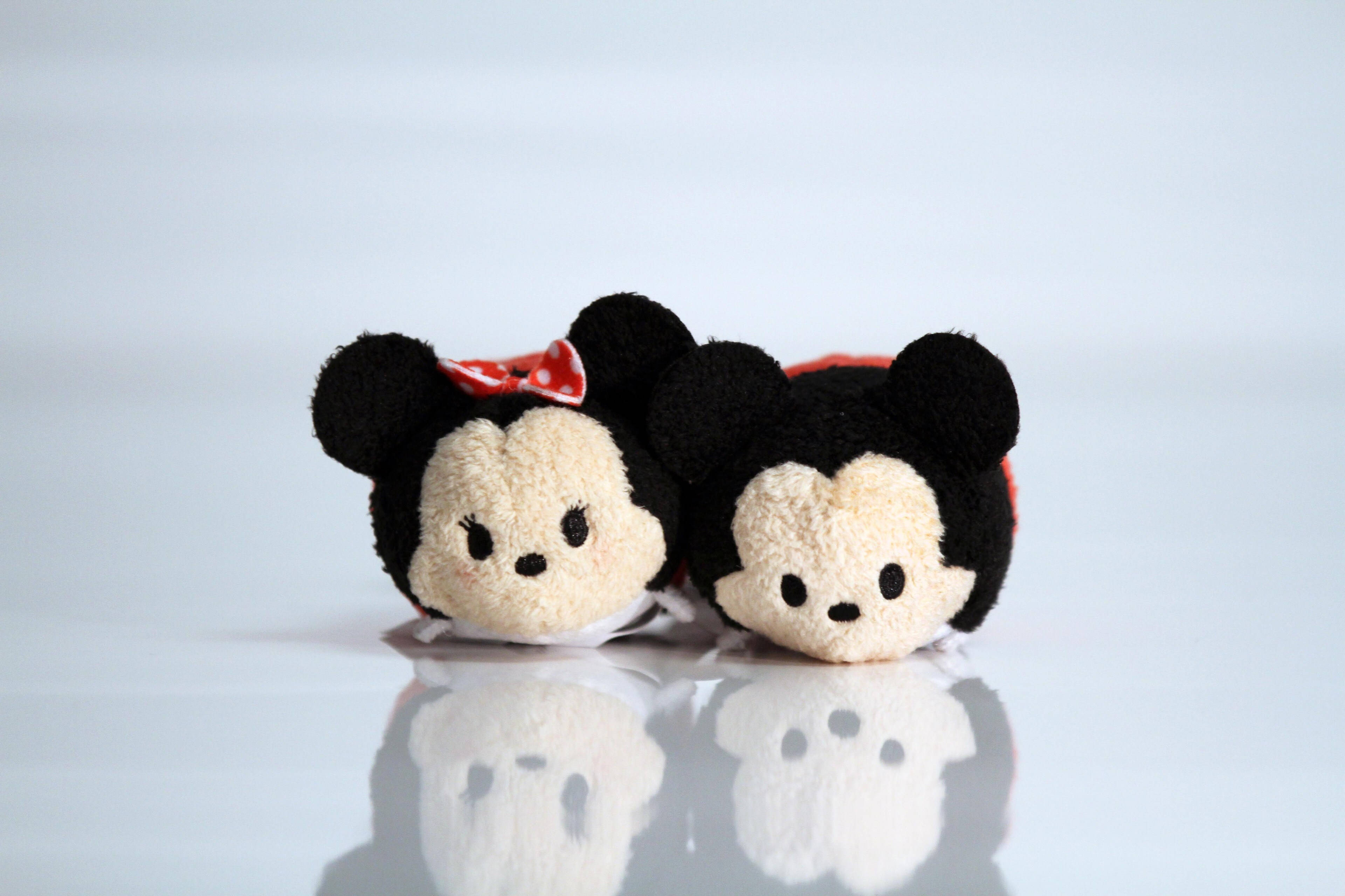 Tsum Tsum 情侶組合 壁紙 — 兩個可愛的Tsum Tsum毛公仔米奇和米妮並排躺在反光的白色表面上。