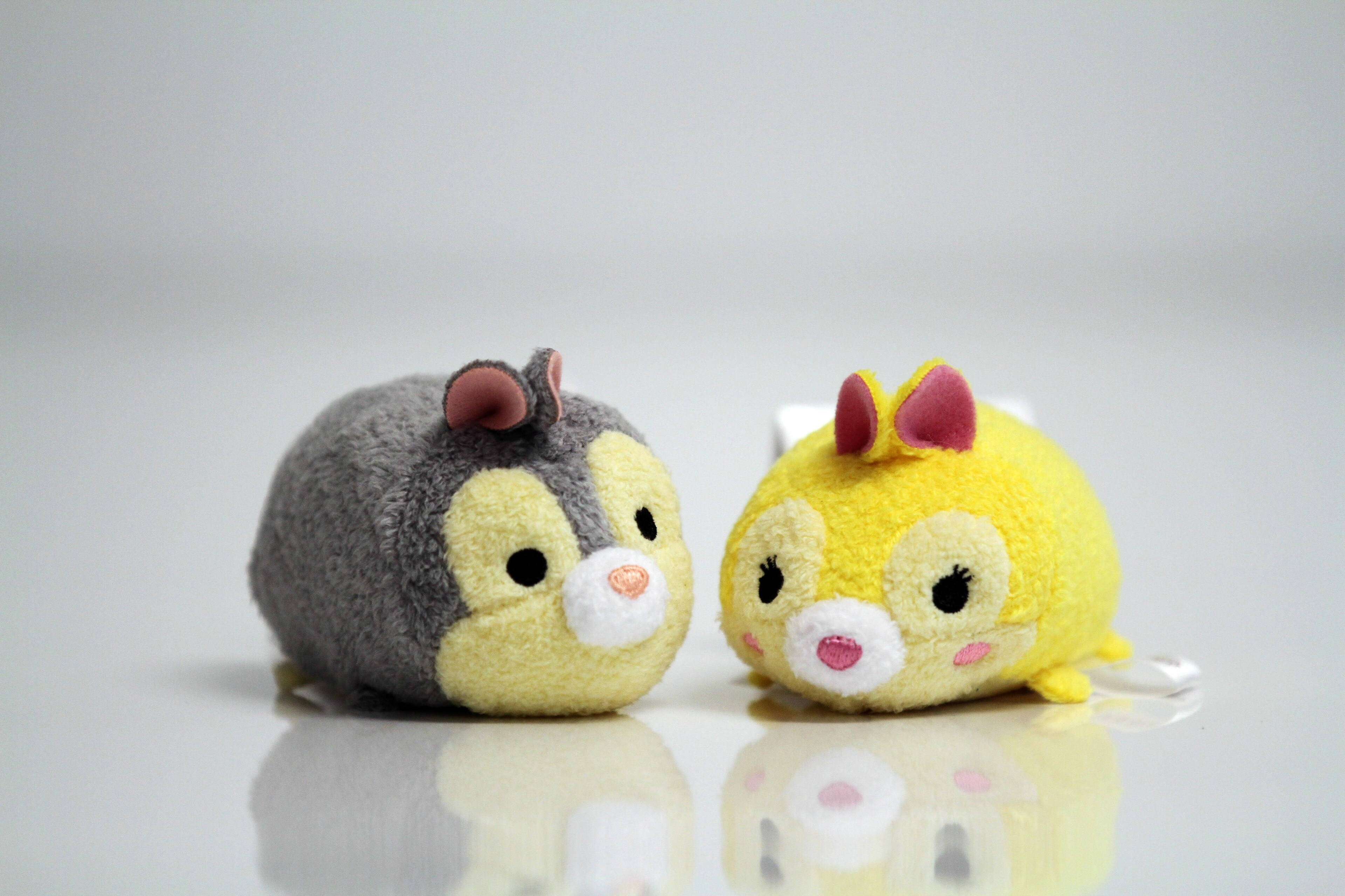 Tsum Tsum 救難小隊 壁紙 — 兩個可愛的Tsum Tsum毛絨公仔，一個灰色一個黃色，並排坐在反光的白色表面上。