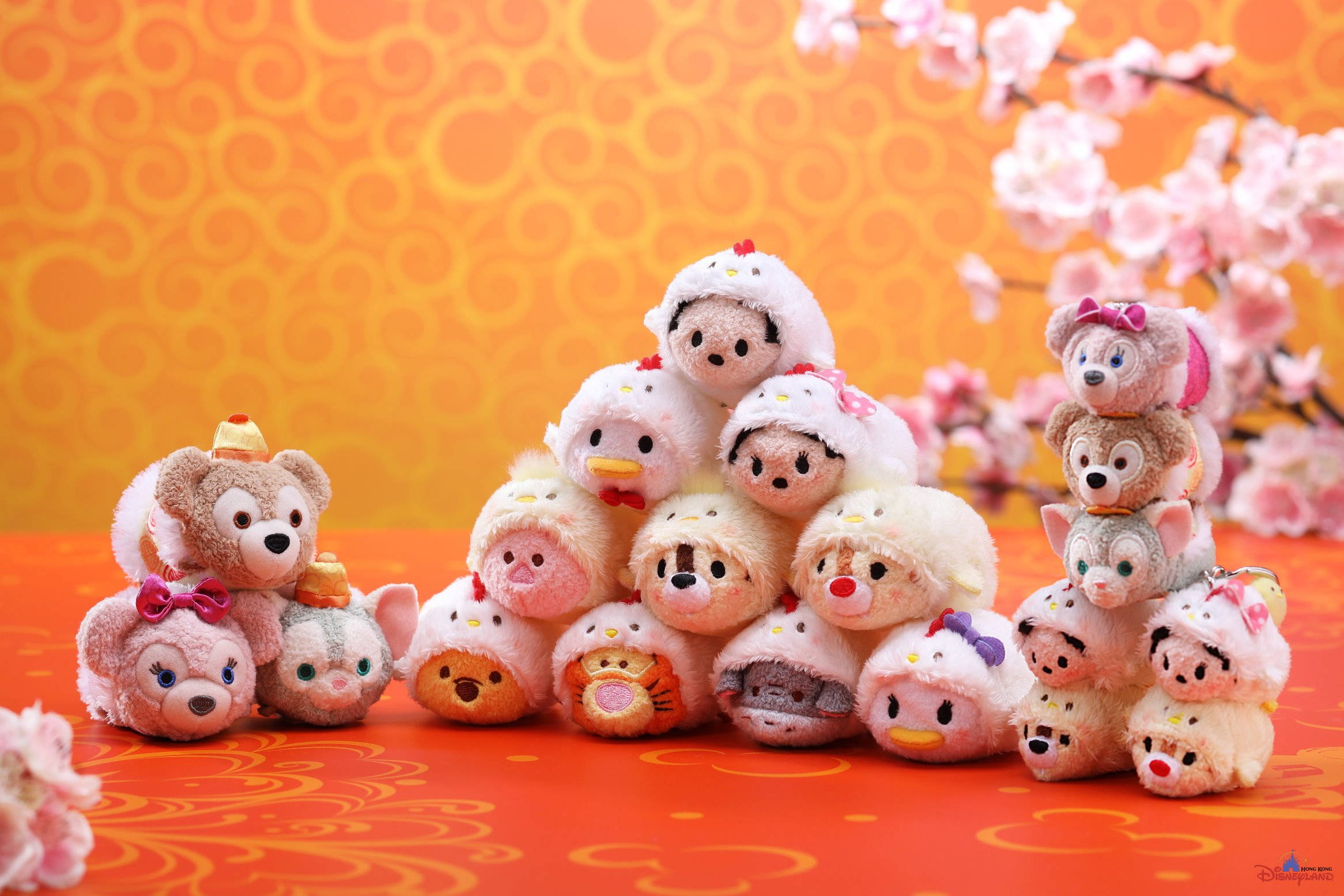 Tsum Tsum 櫻花 壁紙 — 一個由可愛的Tsum Tsum毛絨角色組成的金字塔，穿著節日服裝，背景是溫暖的橙色和櫻花。