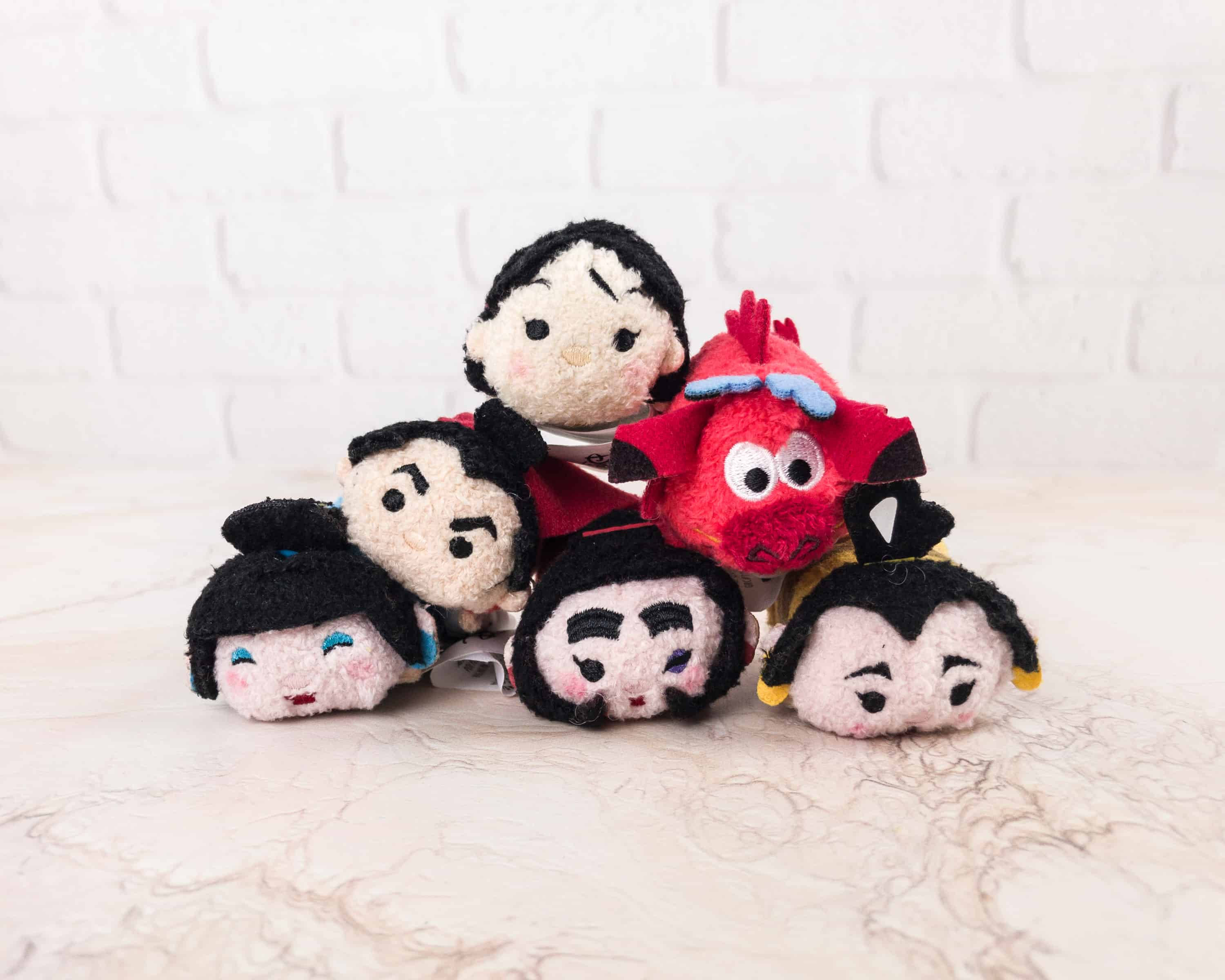Tsum Tsum 花木蘭 壁紙 — 一堆表情各異的迪士尼 Tsum Tsum 毛絨公仔放在大理石表面上，背景是白色磚牆。