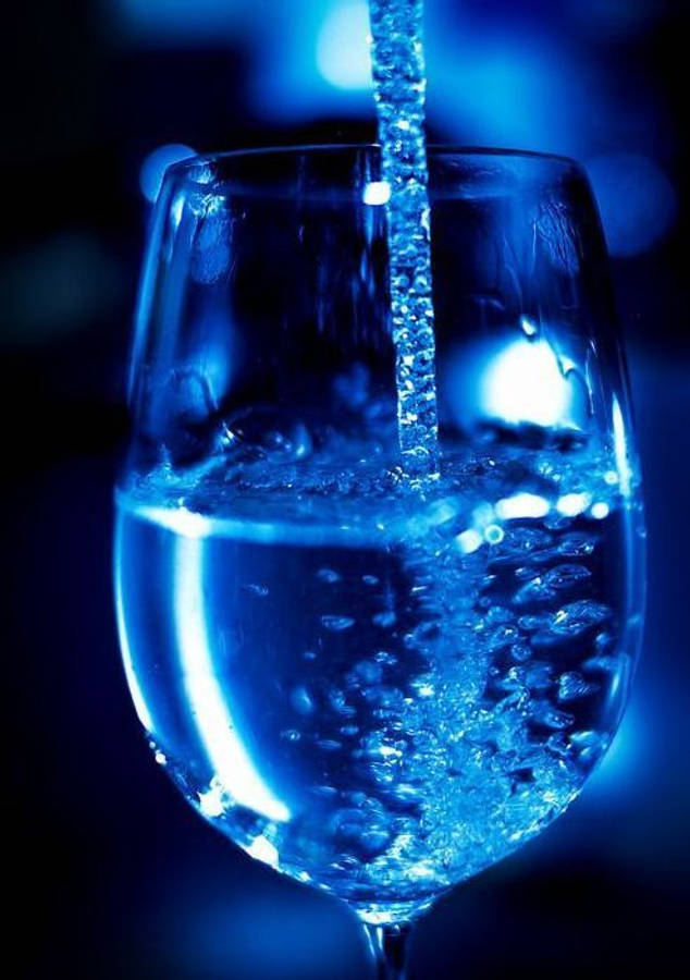 深藍色系Tumblr風格水杯壁紙 壁紙 — 在清涼藍光下，氣泡水倒入玻璃杯的特寫，帶有鮮明的氣泡和反射。